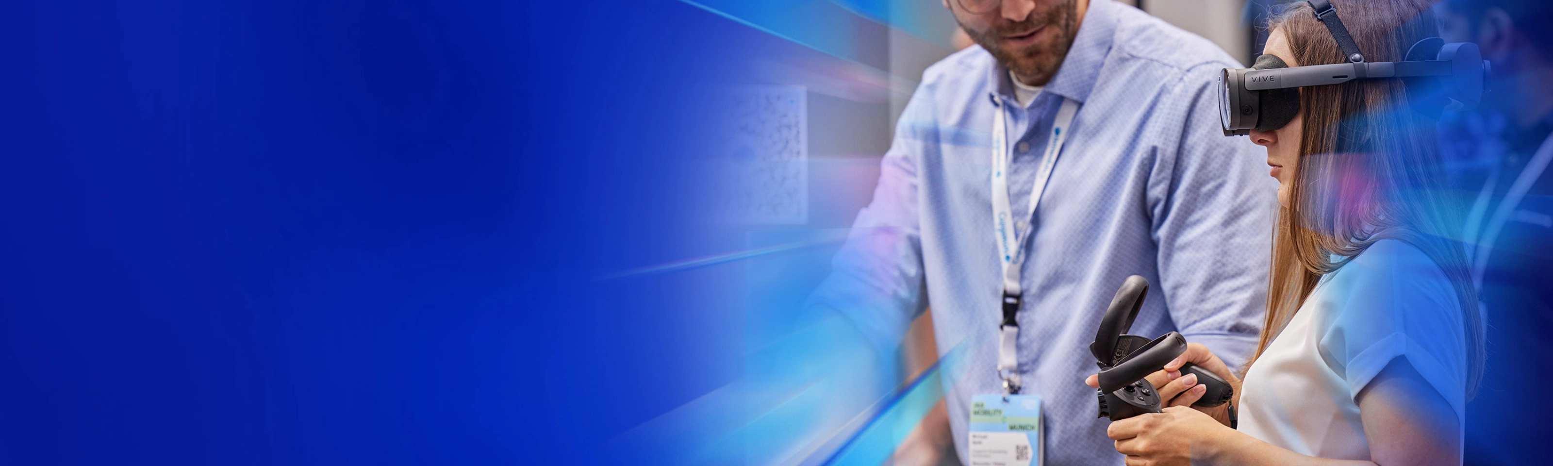 Frau testet VR-Brille mit Controller, daneben steht ein Mann an einem Messestand.