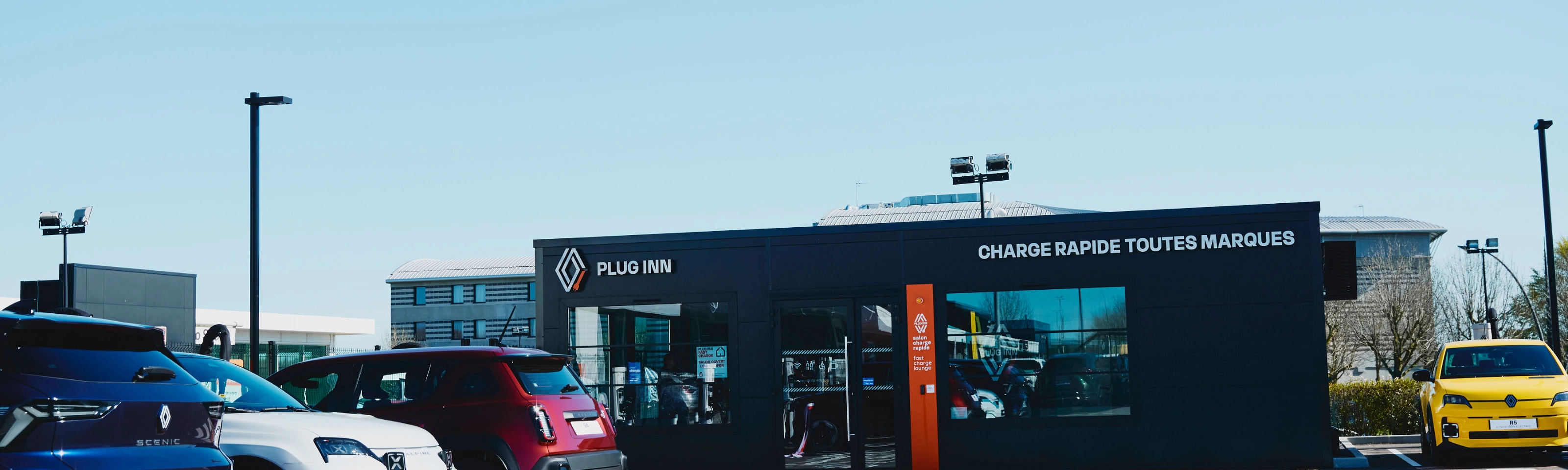 Außenansicht einer Plug-Inn-Schnellladestation mit mehreren geparkten Autos.
