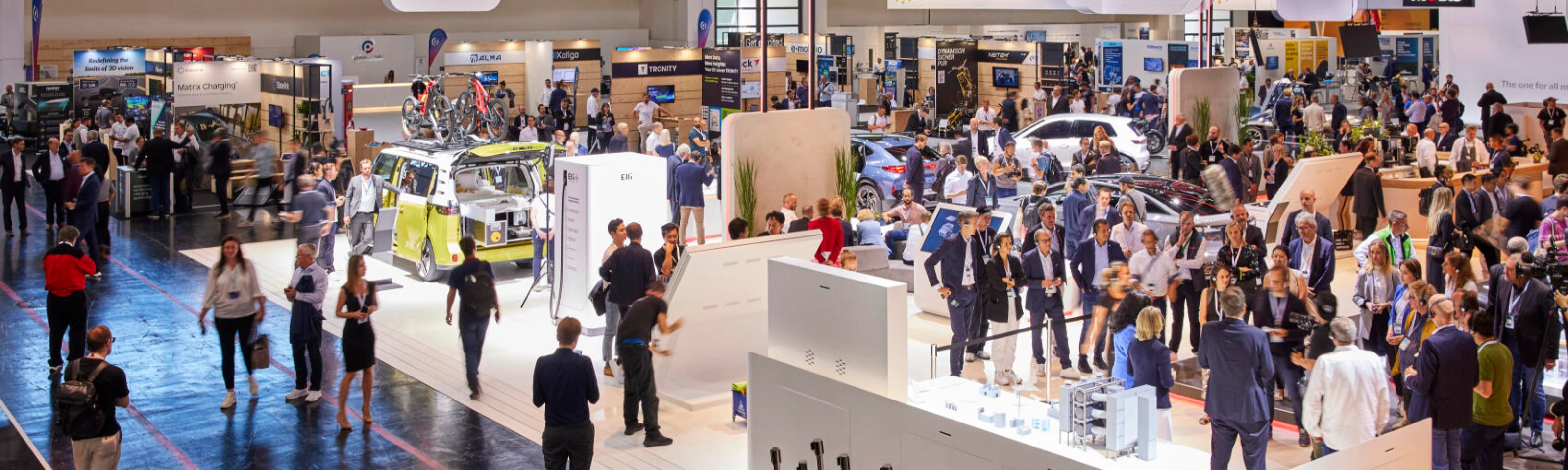Busy exhibition hall at IAA Mobility 2023 featuring multiple booths, vehicles, and technology displays, with many visitors engaging and walking through the space.
