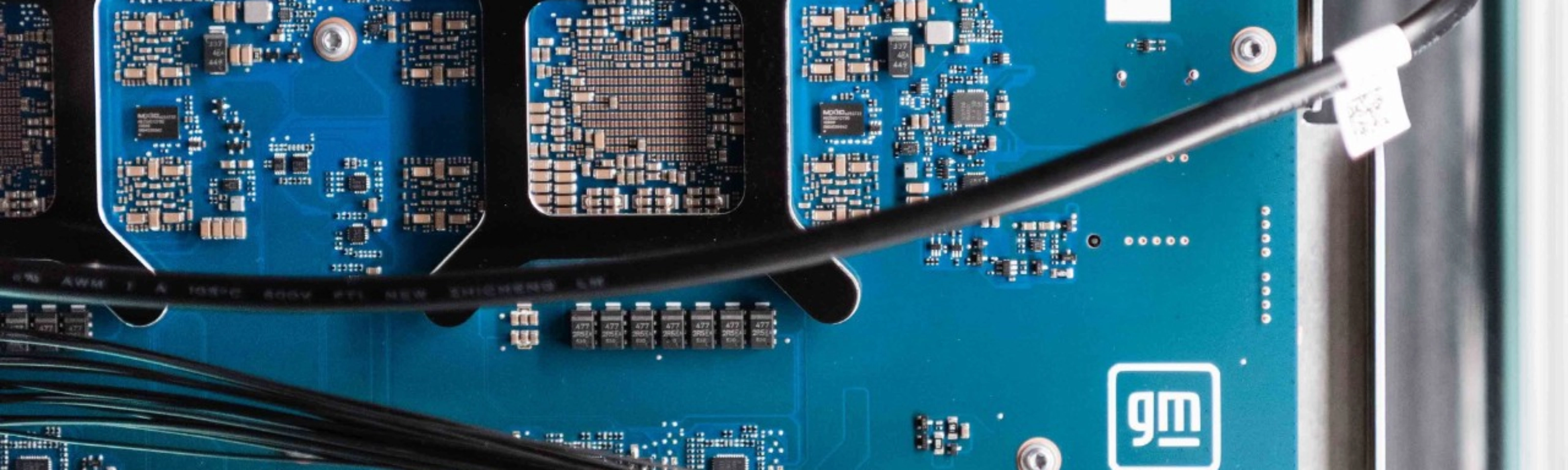 Close-up of a blue General Motors circuit board with electronic components and connectors.