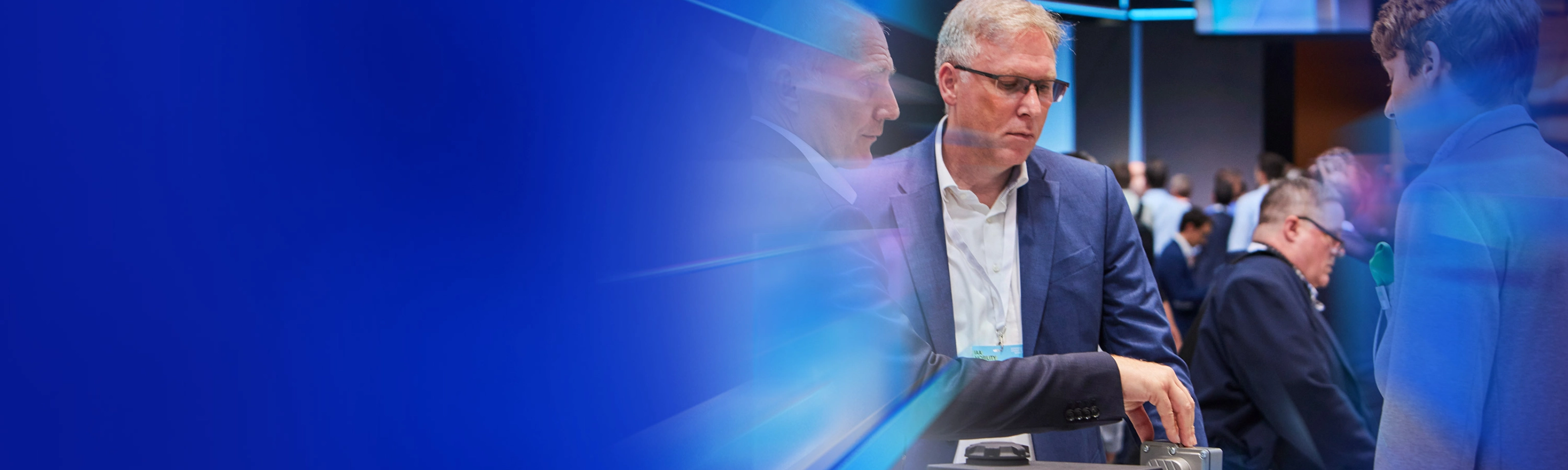Drei Männer begutachten ein technisches Bauteil auf einer Messe beim IAA Summit.
