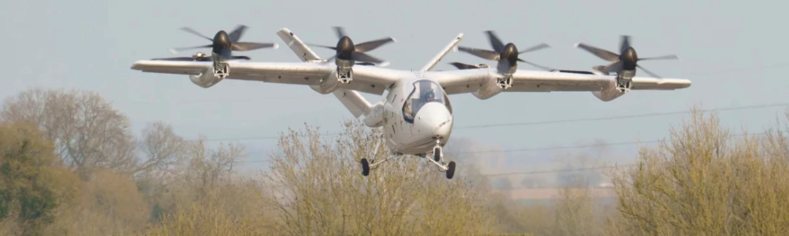 Electric aircraft with multiple rotors flying over trees.