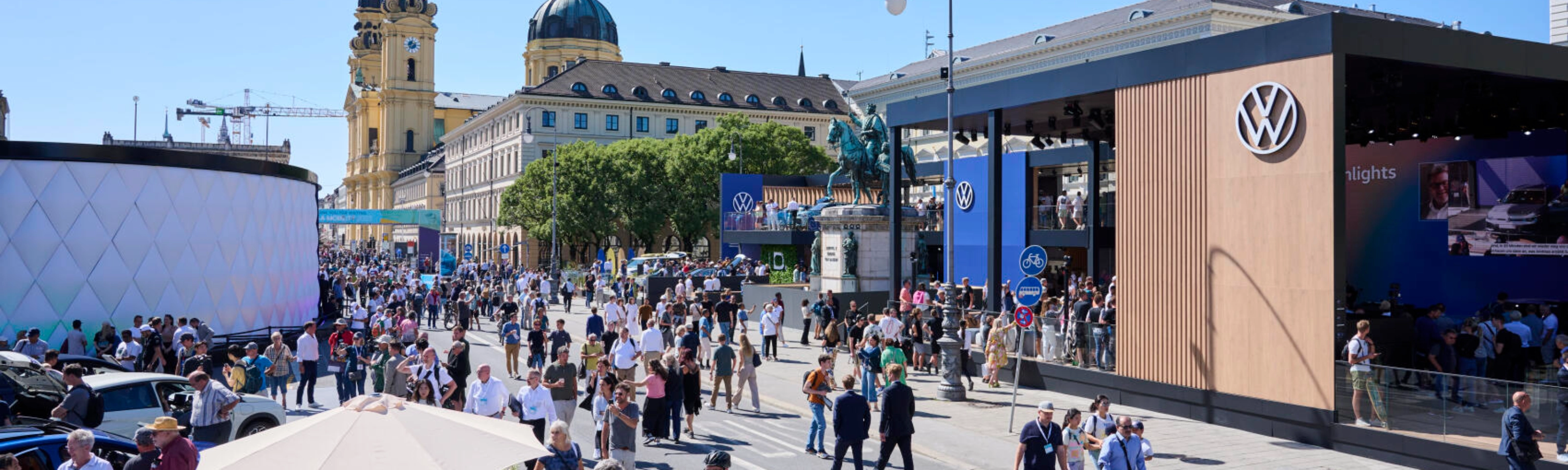 Menschen besuchen eine Outdoor-Mobilitätsmesse mit Ständen und historischen Gebäuden.