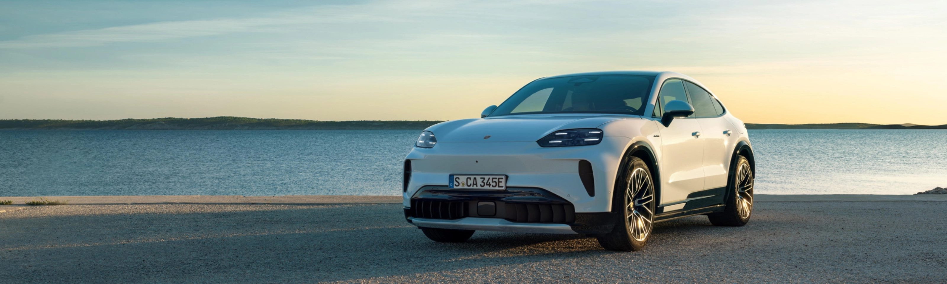 Weißer Porsche steht am Wasser bei Sonnenuntergang.