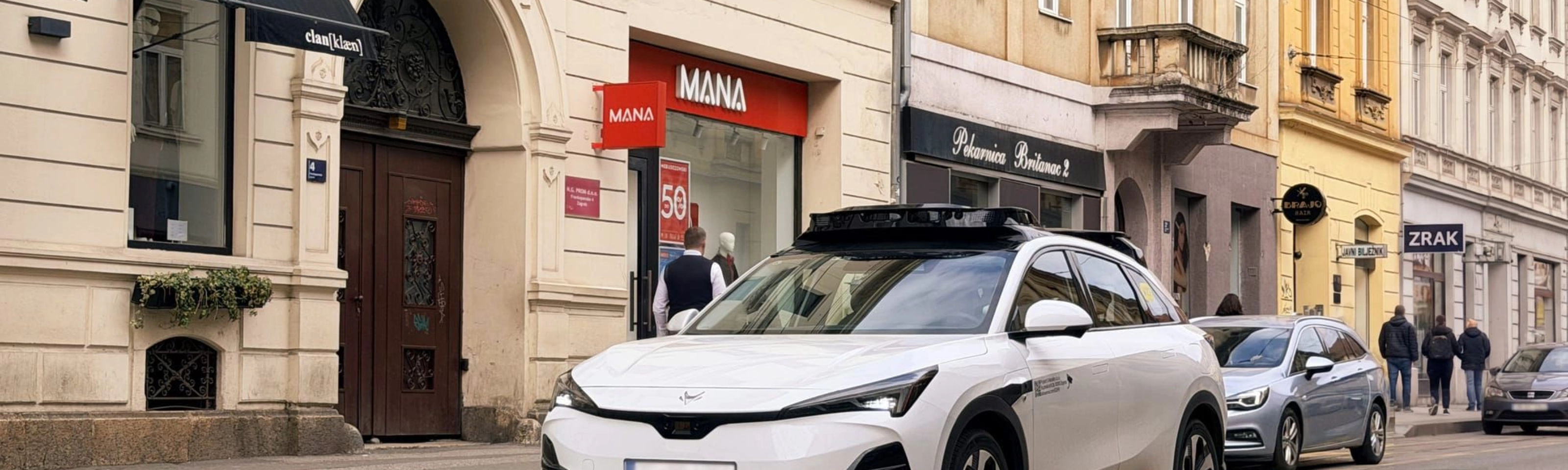 Autonomes Testfahrzeug fährt durch eine Stadtstraße mit Geschäften