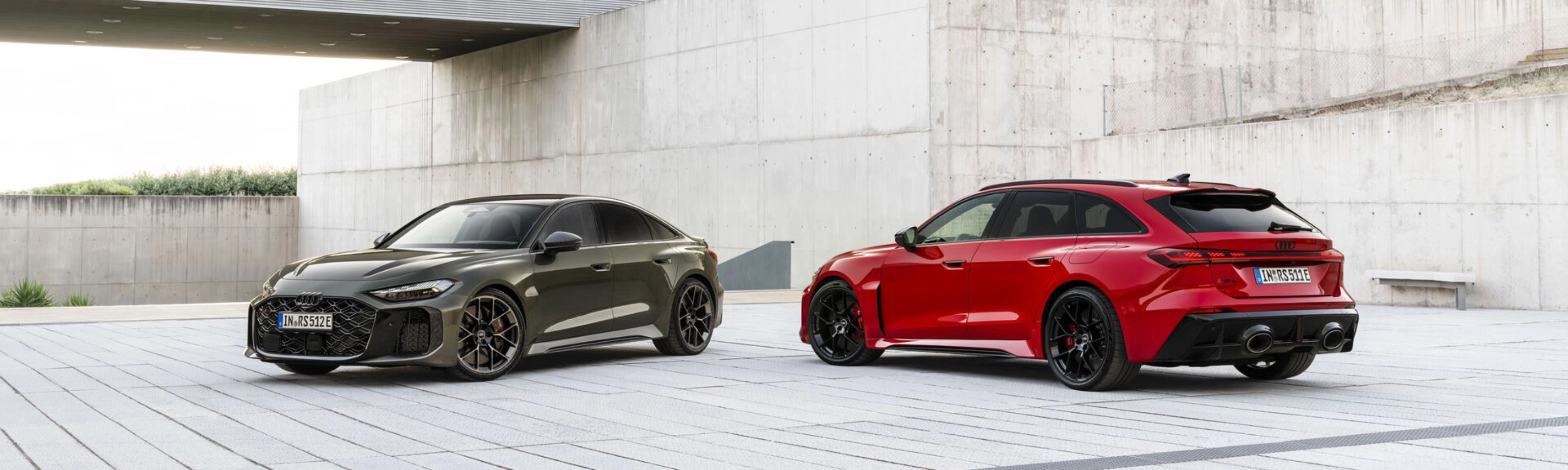 Two Audi performance cars parked in a modern concrete courtyard.