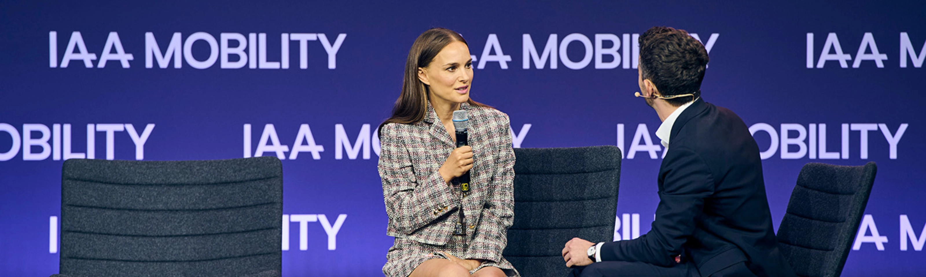 Natalie Portman bei einem Live-Bühneninterview auf der IAA Mobility, sitzend neben einem Moderator vor einer Bühne mit Veranstaltungslogo.
