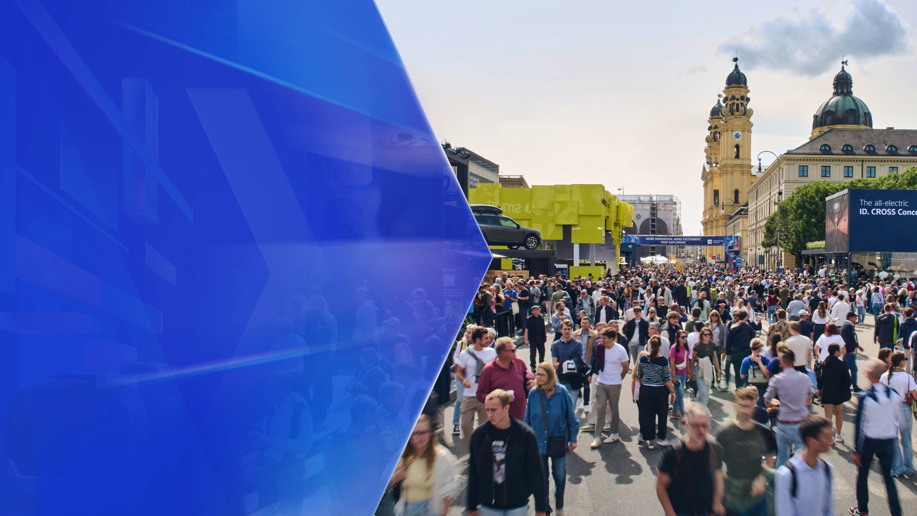 Große Menschenmenge auf einer Mobilitätsmesse im Freien mit Ausstellungsständen und Altbauten.