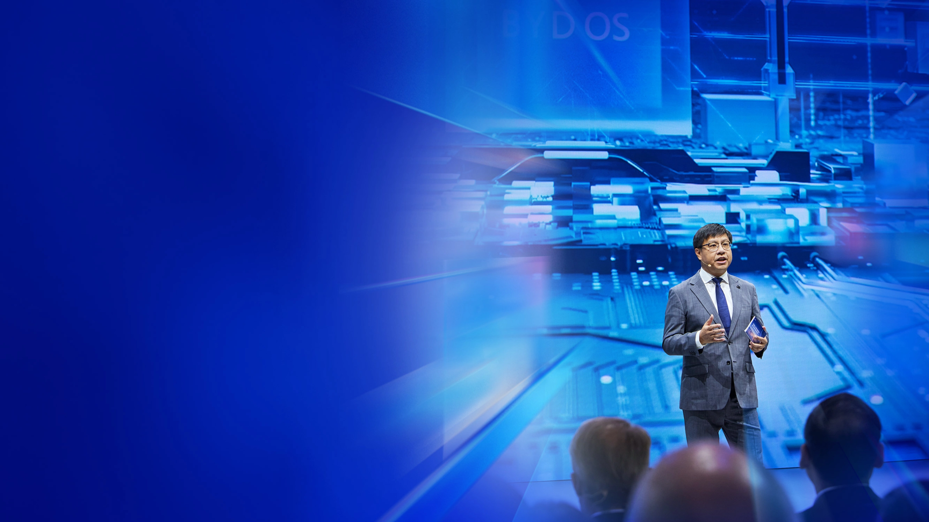 Ein Redner im Anzug spricht auf der IAA Summit Bühne vor digitalem Schaltkreis-Hintergrund.