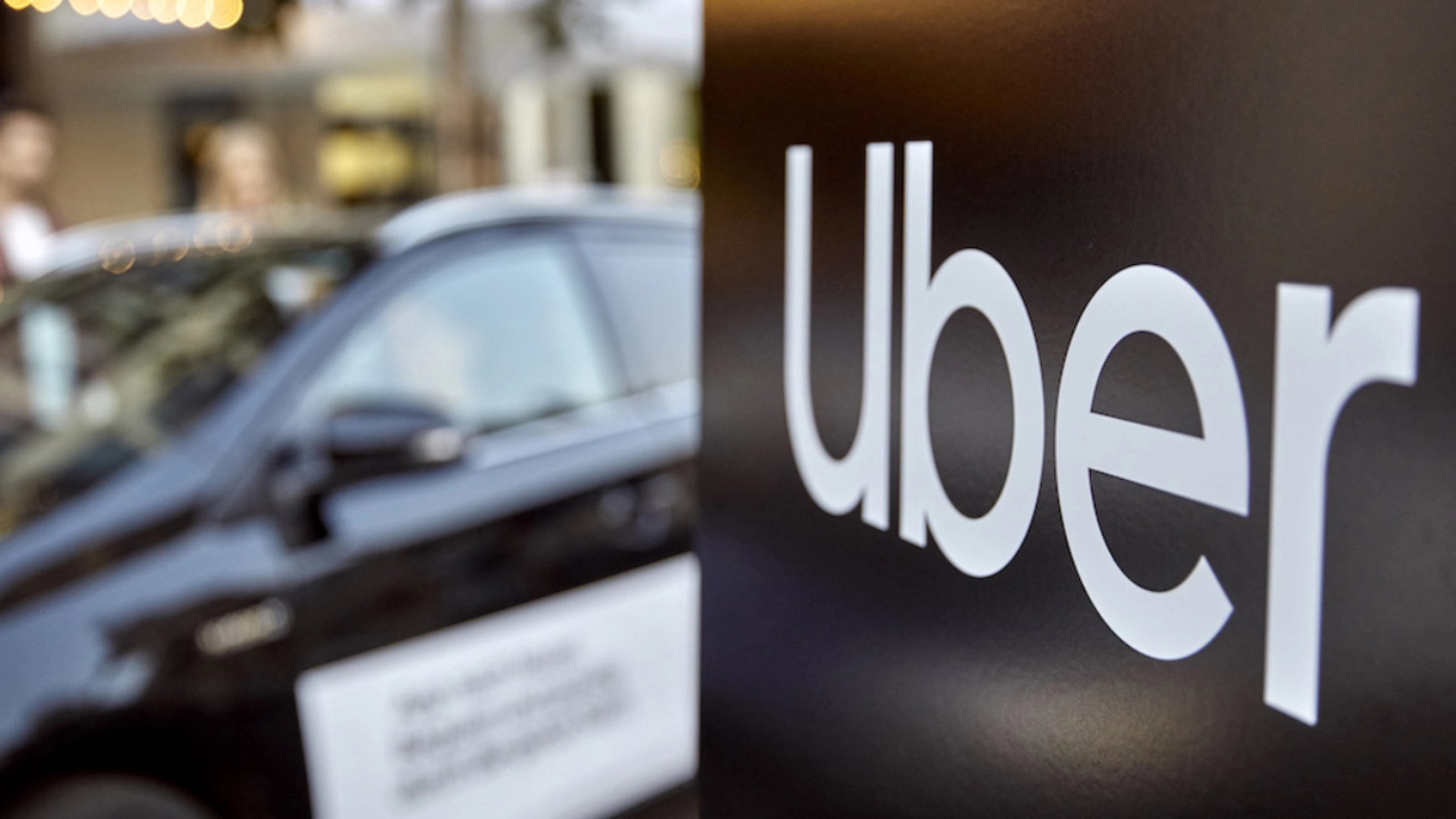 Uber-Logo auf einem Schild, dahinter unscharf ein Auto.