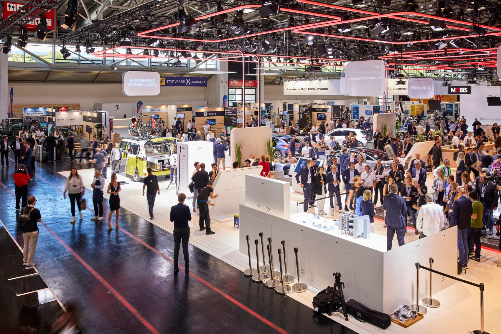 Crowds of visitors walk through a large exhibition hall at the IAA Mobility, with booths showcasing vehicles, technology innovations, and mobility concepts under bright lighting.