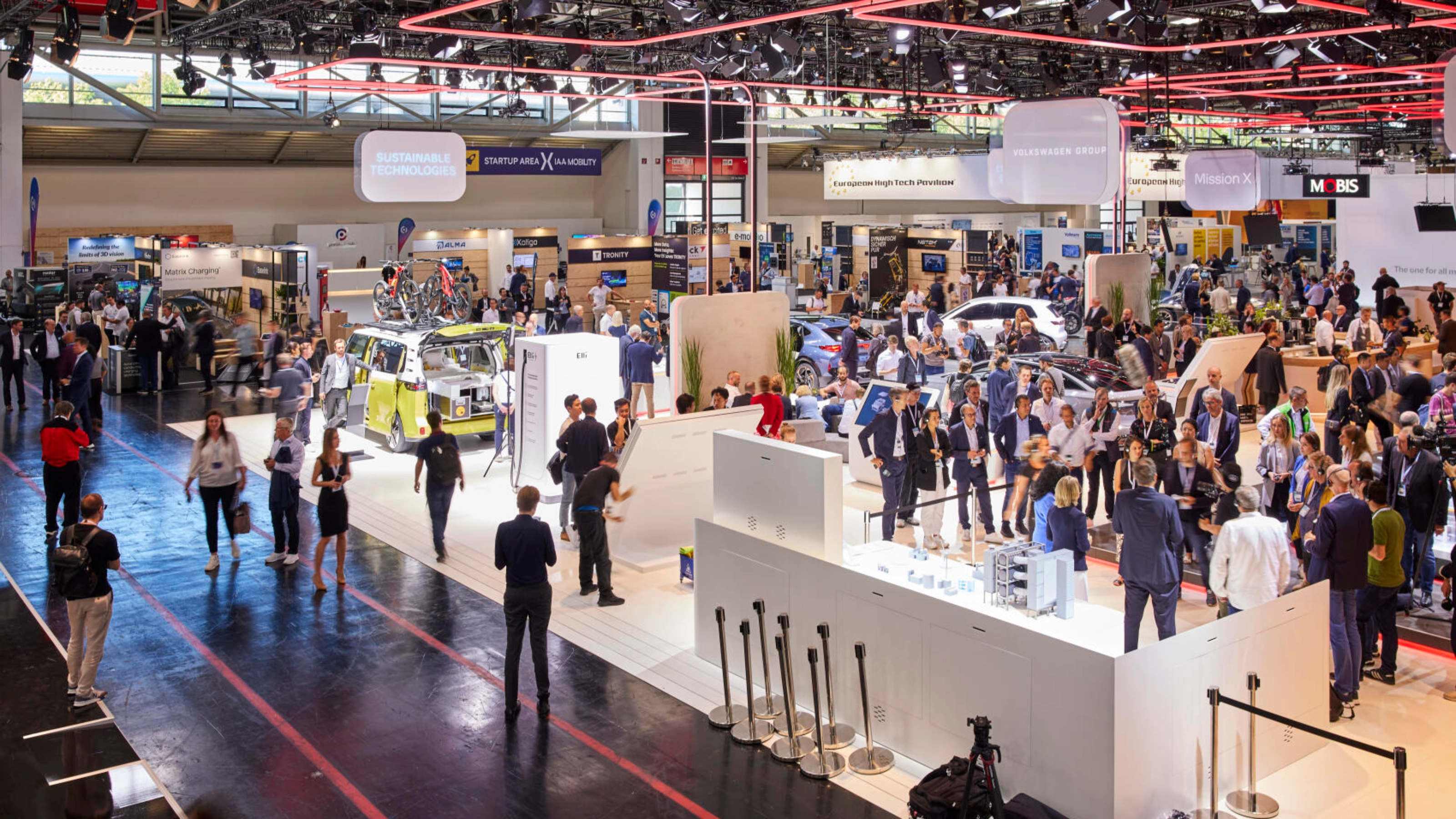 Busy exhibition hall at IAA Mobility 2023 featuring multiple booths, vehicles, and technology displays, with many visitors engaging and walking through the space.