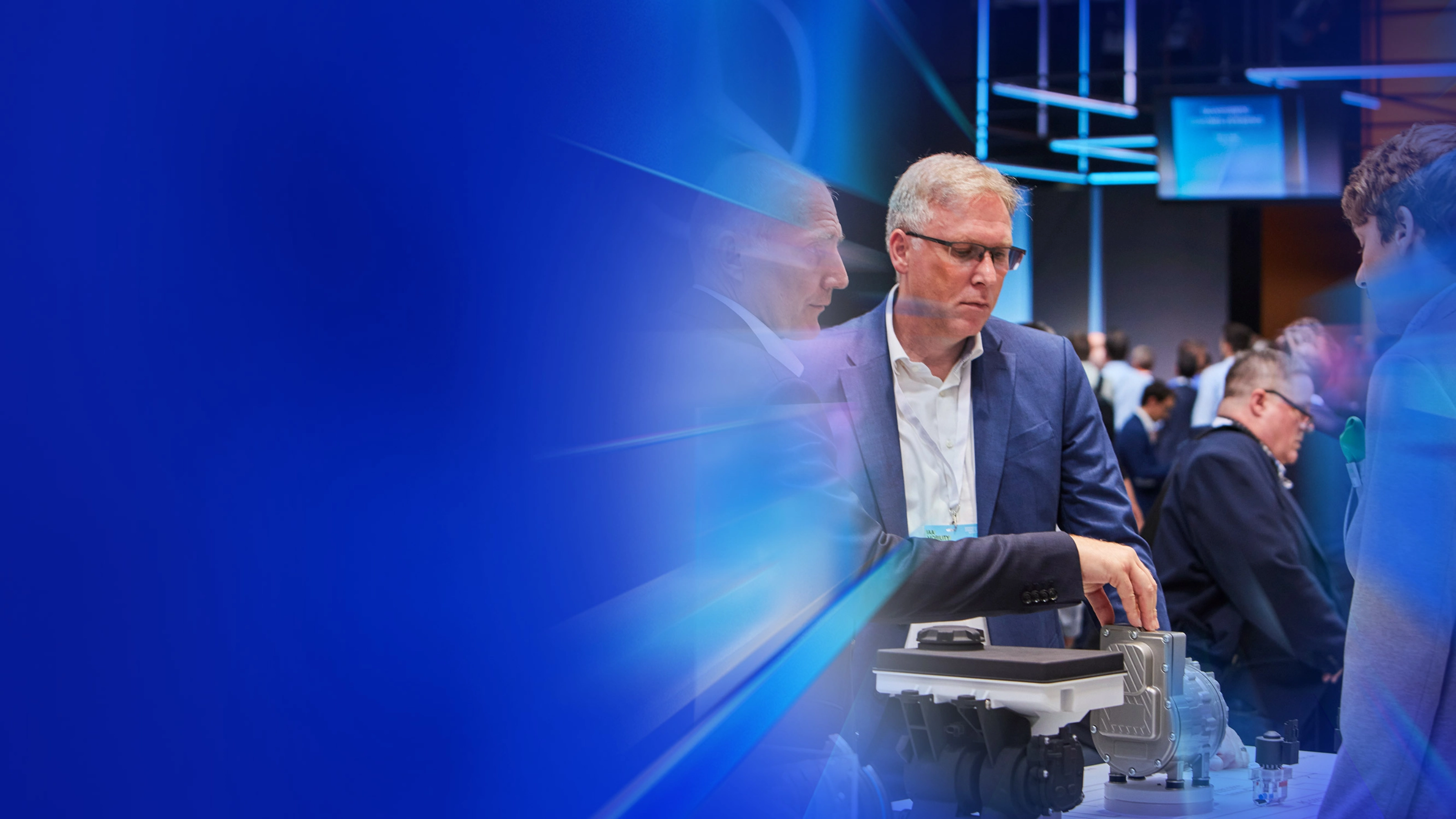 Drei Männer begutachten ein technisches Bauteil auf einer Messe beim IAA Summit.