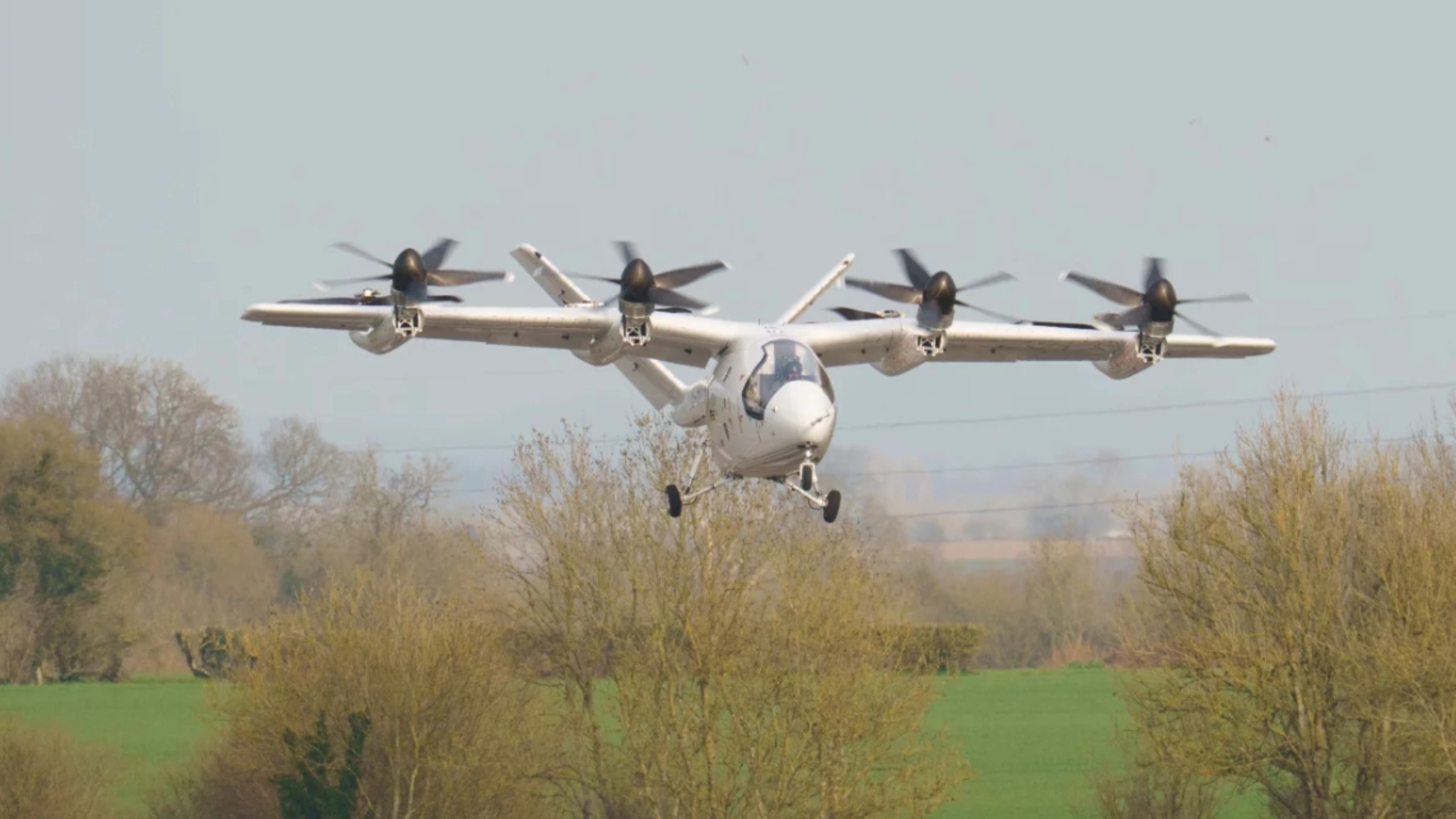 Electric aircraft with multiple rotors flying over trees.