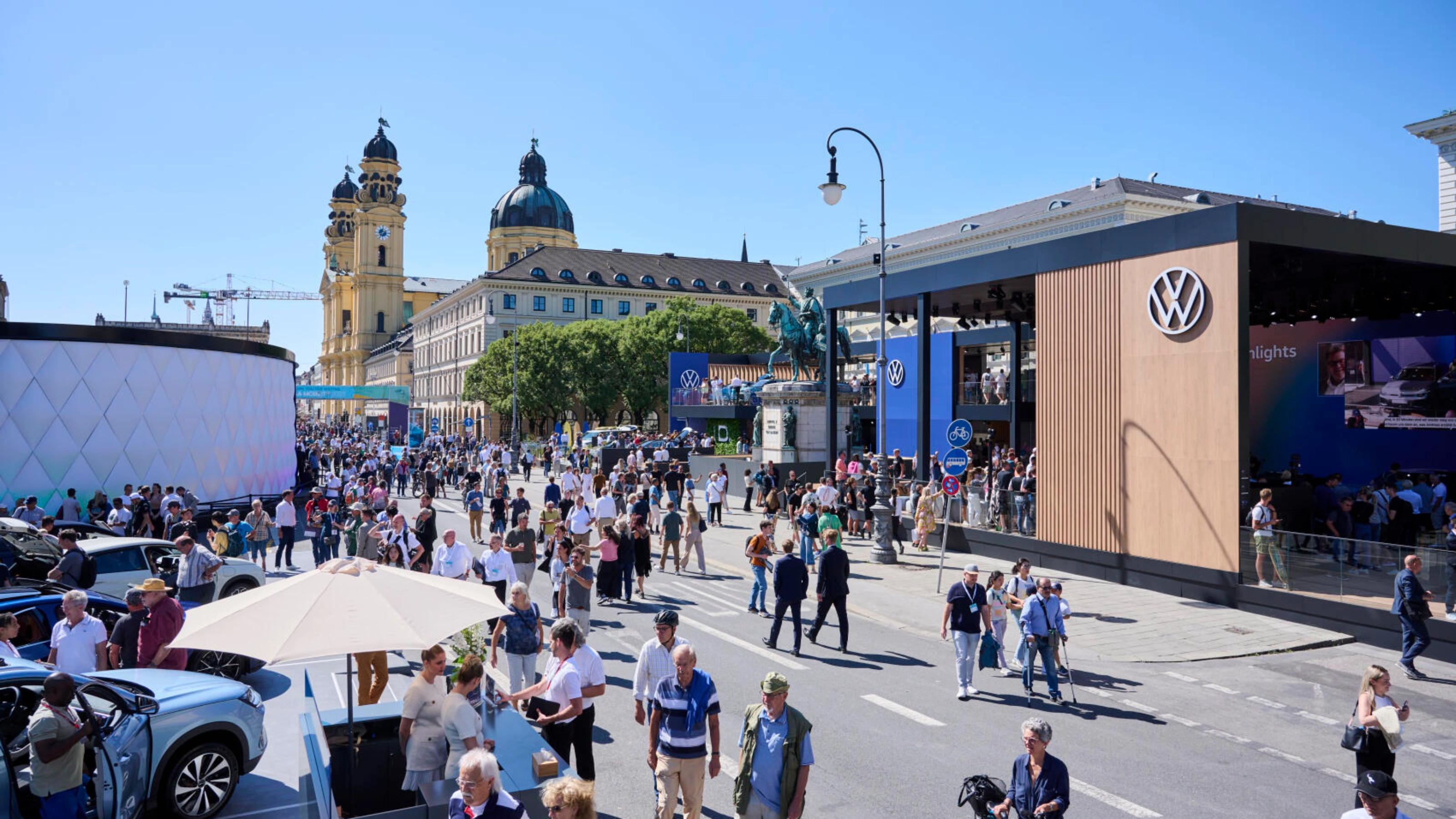 Menschen besuchen eine Outdoor-Mobilitätsmesse mit Ständen und historischen Gebäuden.