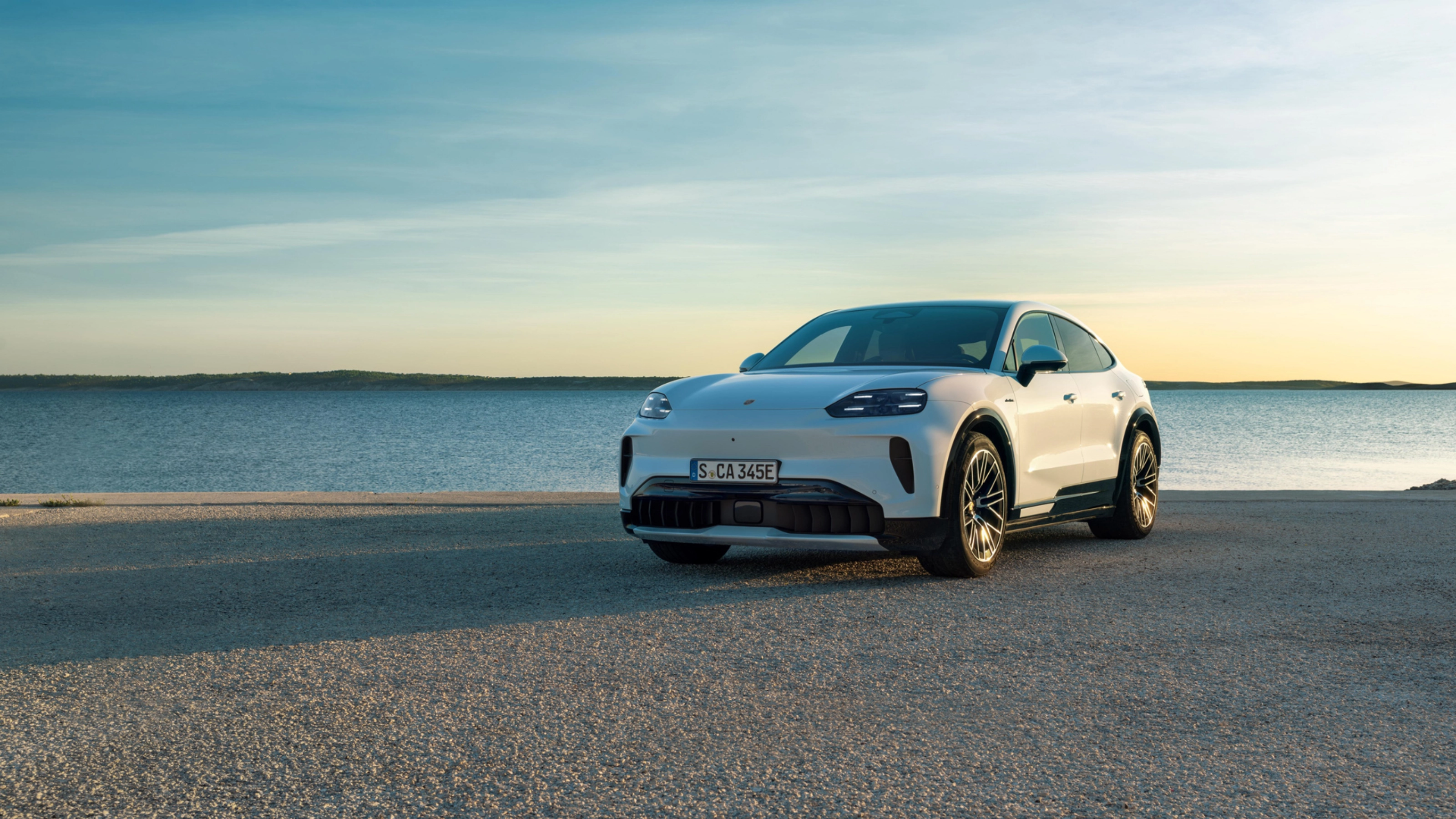 Weißer Porsche steht am Wasser bei Sonnenuntergang.