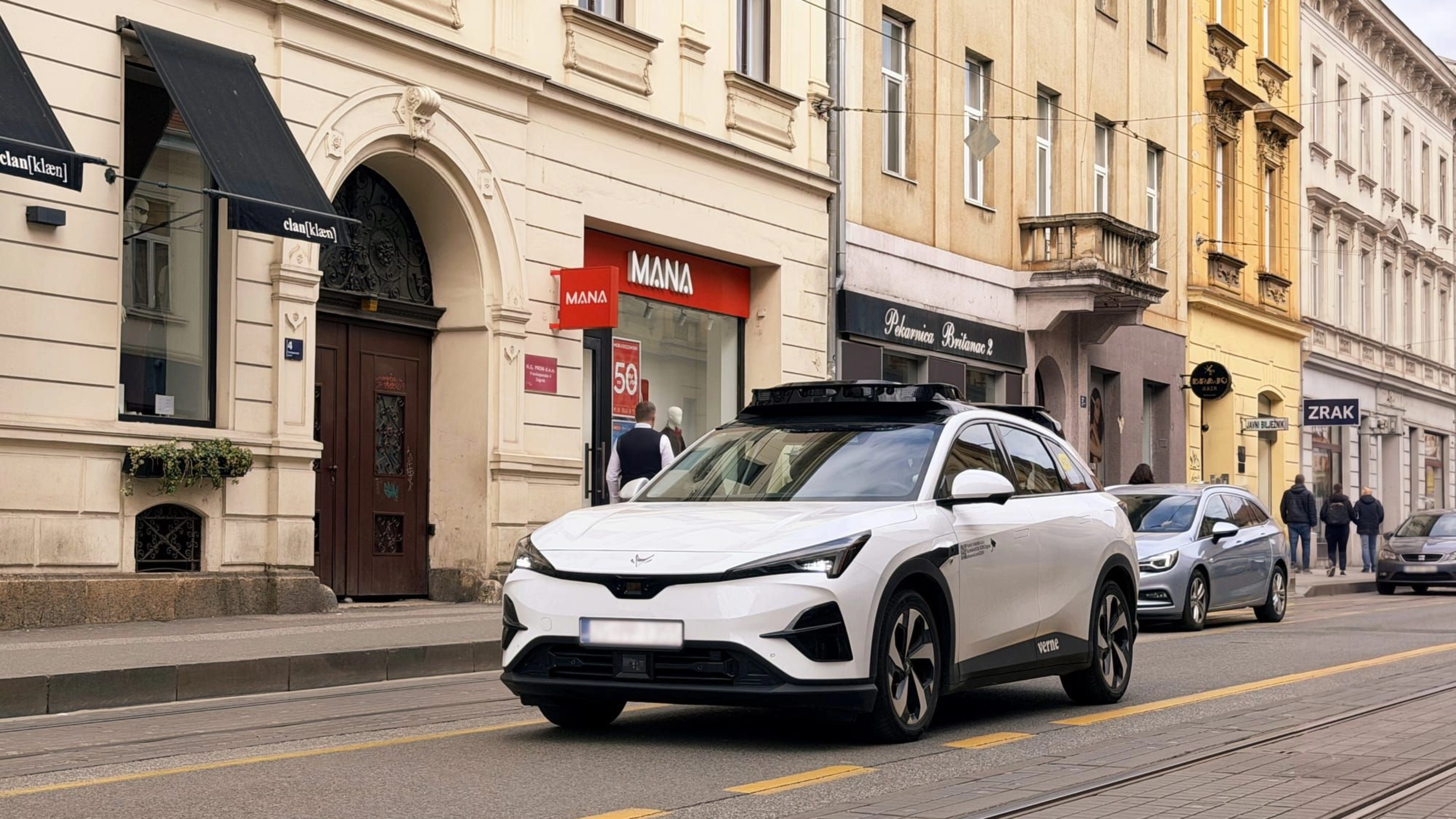 Autonomes Testfahrzeug fährt durch eine Stadtstraße mit Geschäften