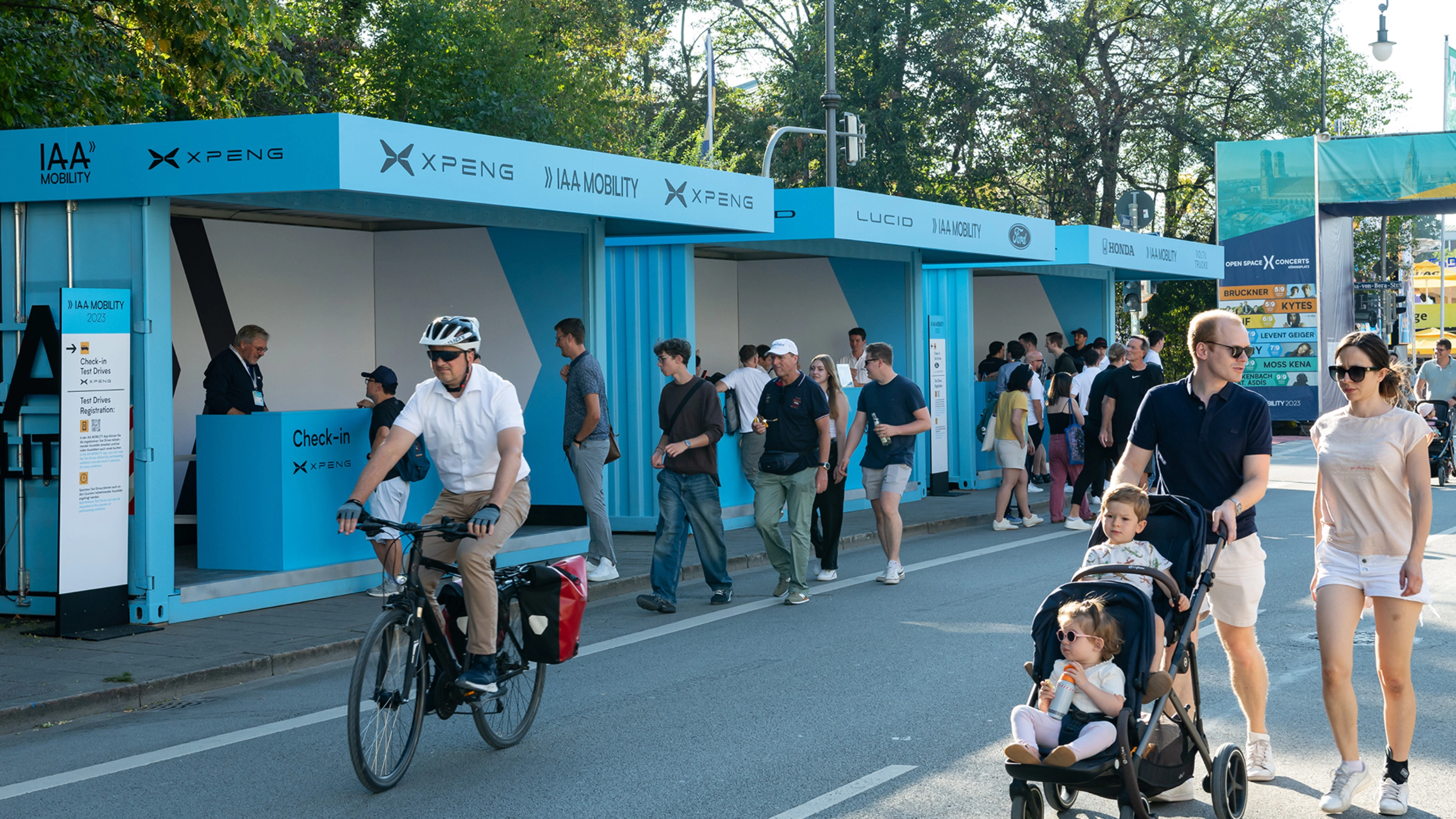 Menschen gehen und fahren mit dem Fahrrad an IAA Mobility Check-in-Ständen auf einer gesperrten Straße vorbei.