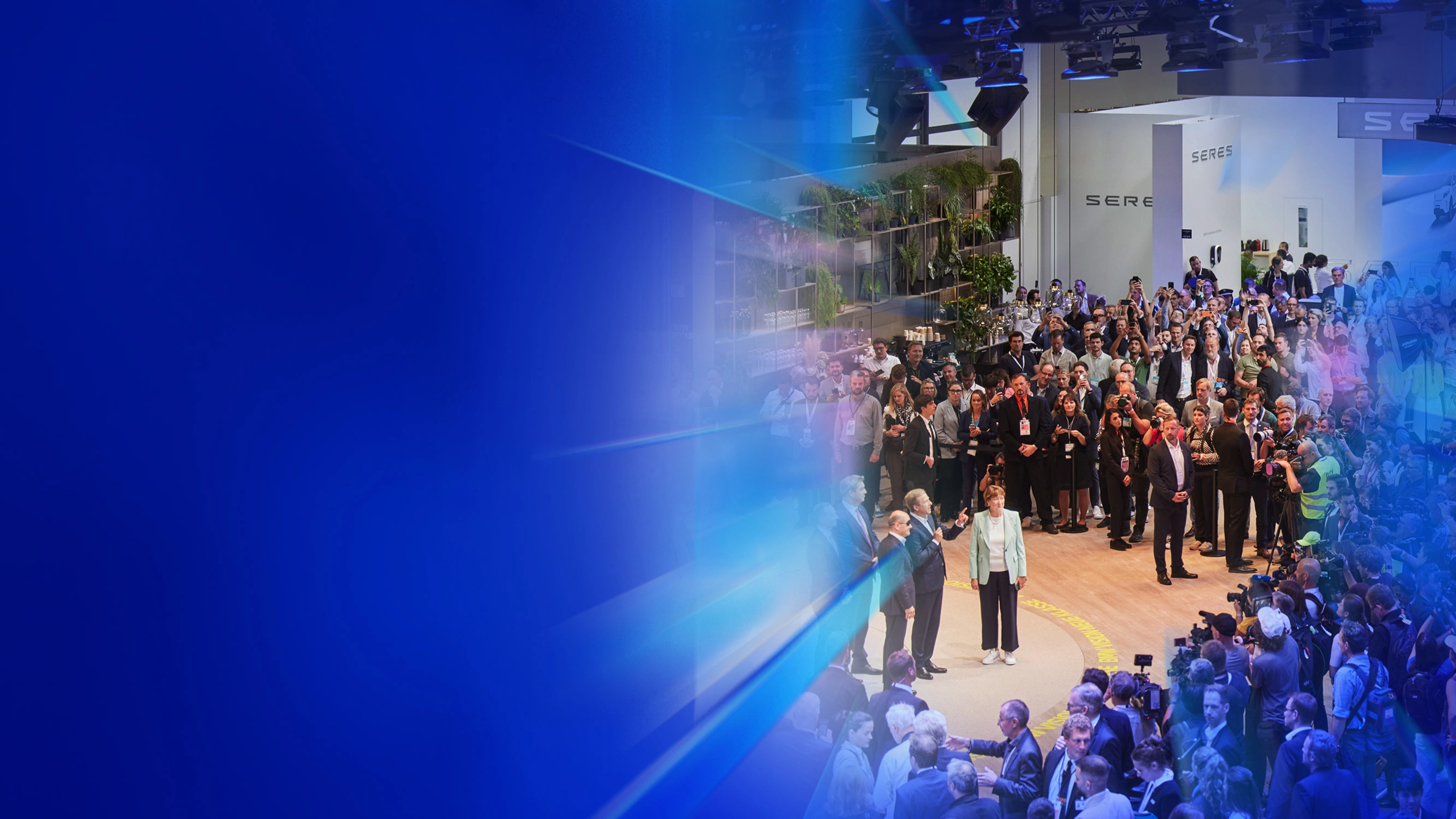 Menschenmenge und Presse auf einer Autoausstellung mit dem Text „5 Gründe – IAA Summit“.