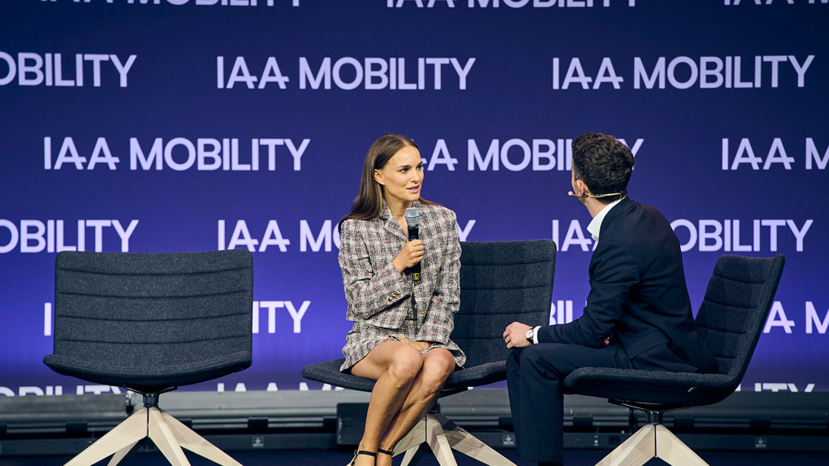 Natalie Portman bei einem Live-Bühneninterview auf der IAA Mobility, sitzend neben einem Moderator vor einer Bühne mit Veranstaltungslogo.