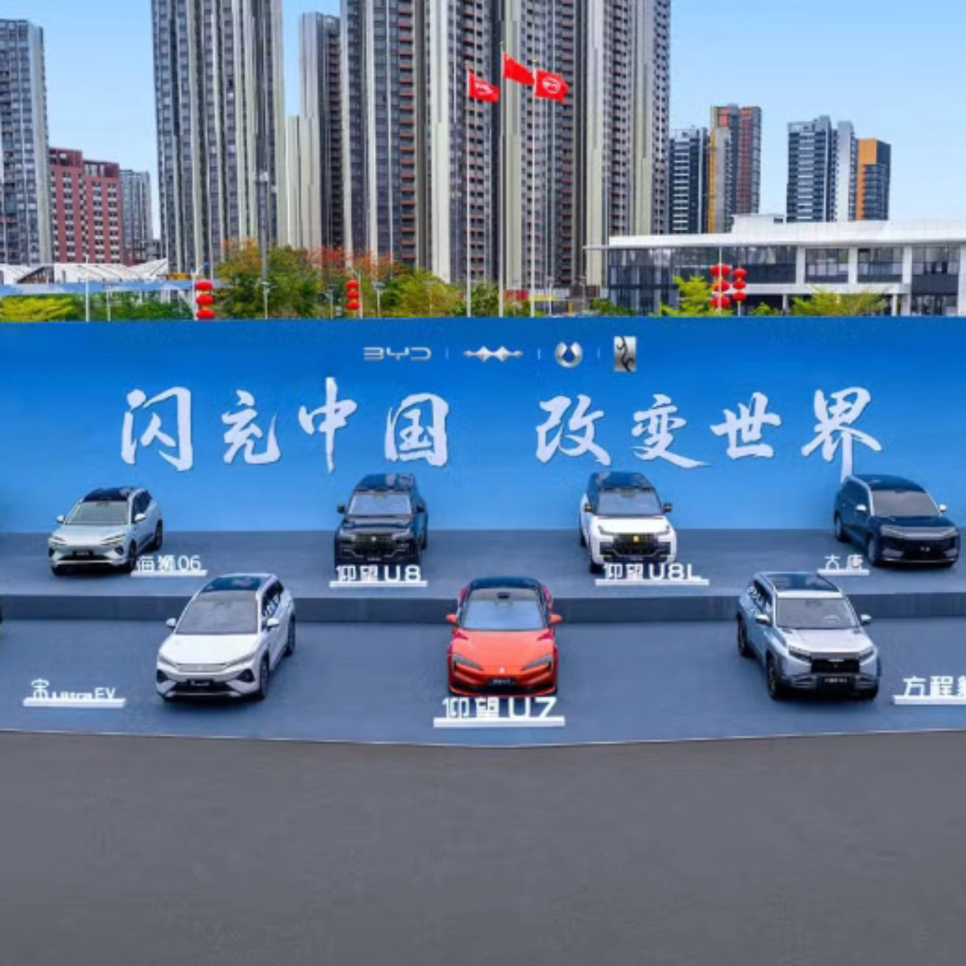 BYD vehicles displayed on a stage outdoors in front of a large promotional backdrop.