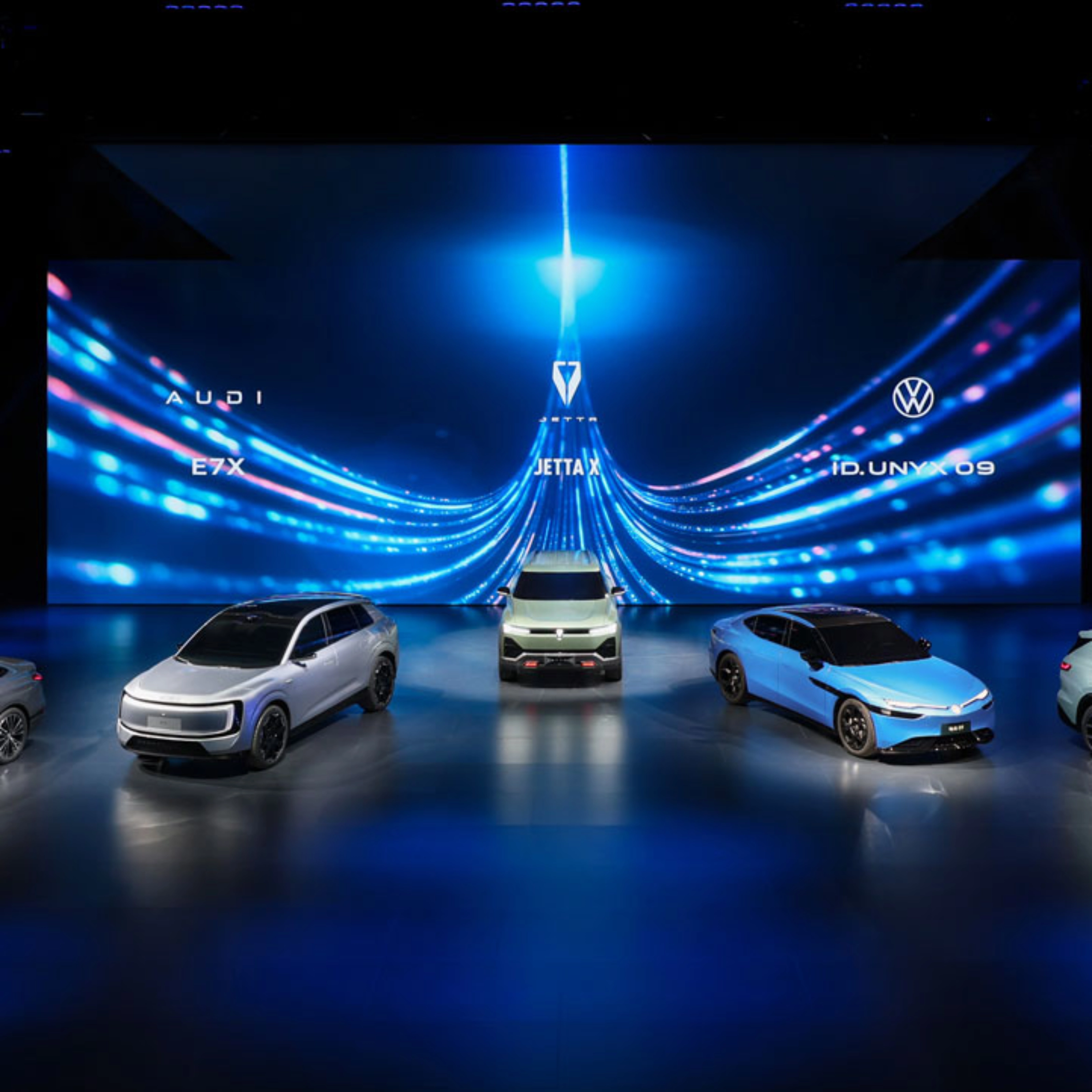Five cars displayed on a stage with blue digital background.