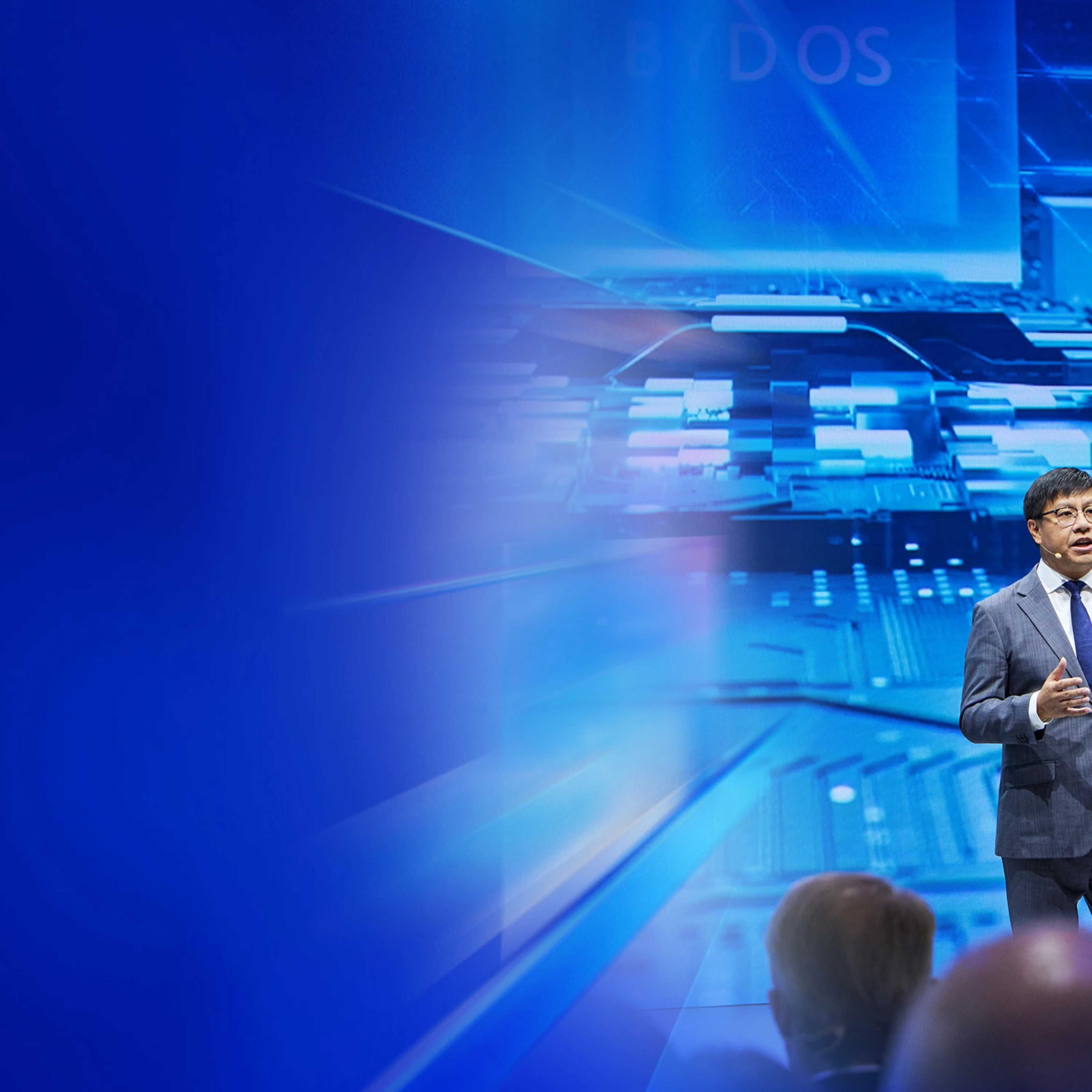 Ein Redner im Anzug spricht auf der IAA Summit Bühne vor digitalem Schaltkreis-Hintergrund.