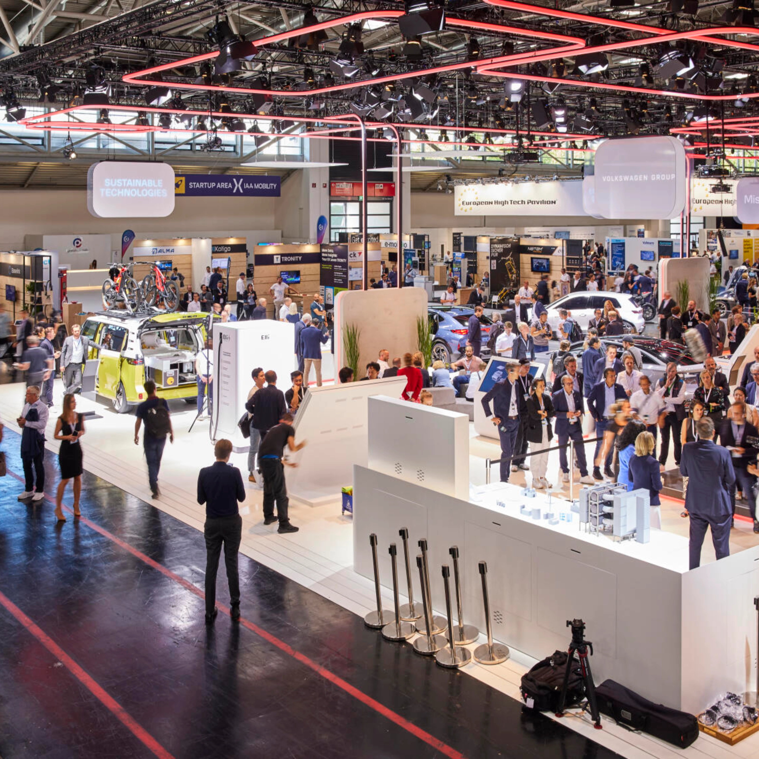 Busy exhibition hall at IAA Mobility 2023 featuring multiple booths, vehicles, and technology displays, with many visitors engaging and walking through the space.