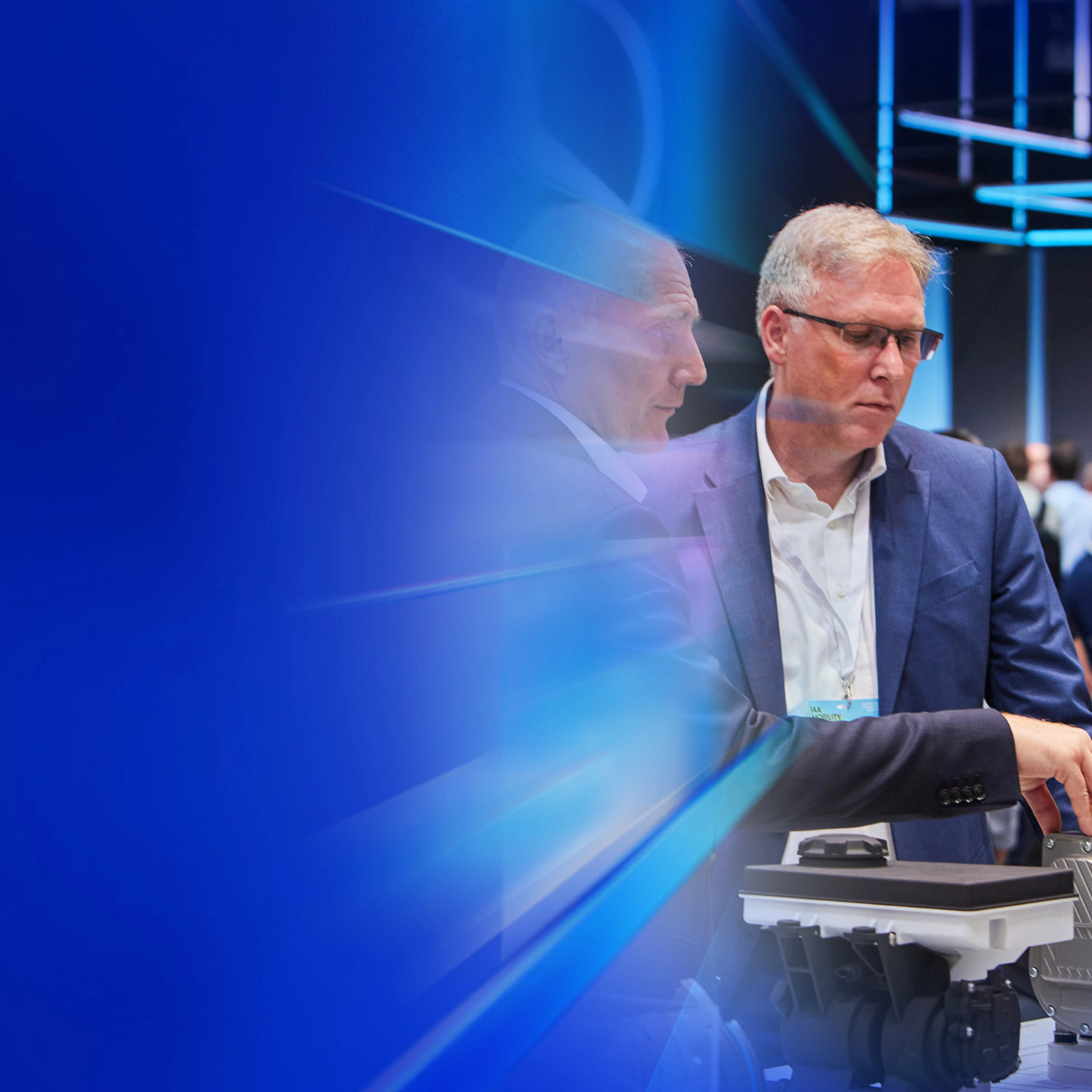 Drei Männer begutachten ein technisches Bauteil auf einer Messe beim IAA Summit.