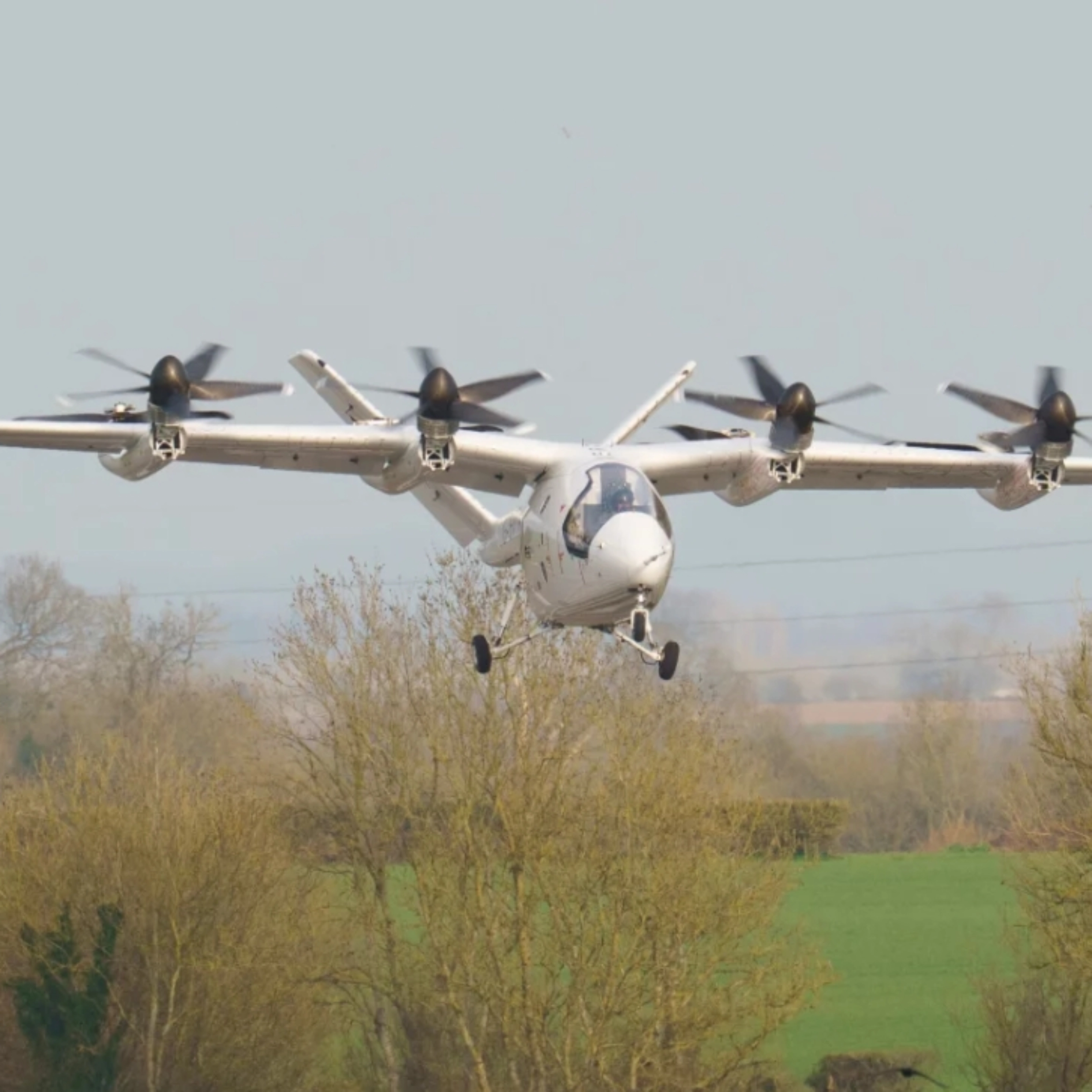Electric aircraft with multiple rotors flying over trees.