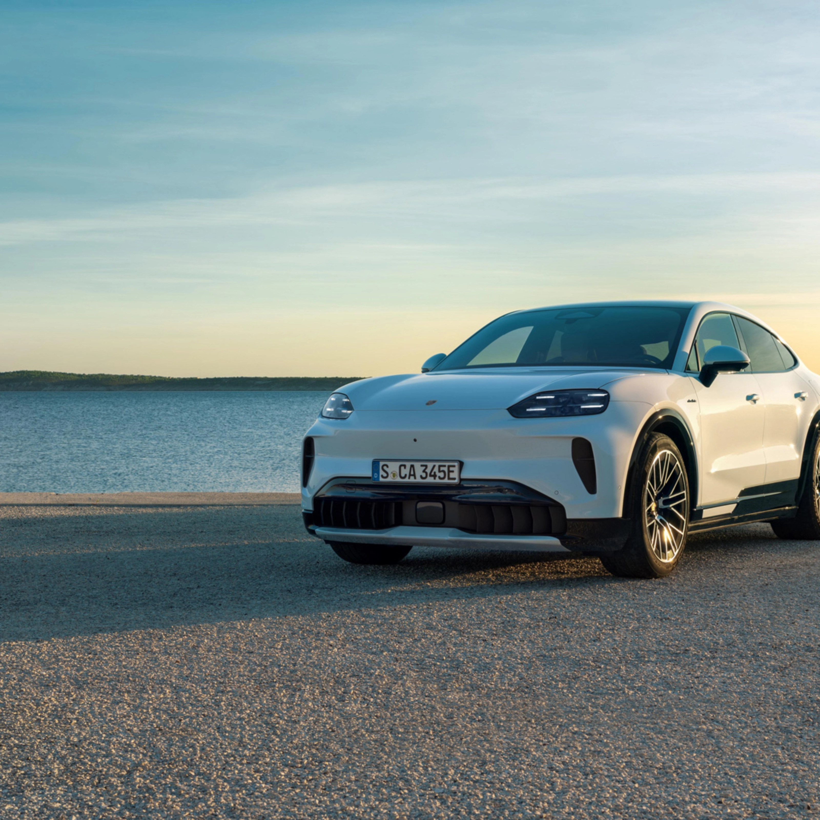 Weißer Porsche steht am Wasser bei Sonnenuntergang.