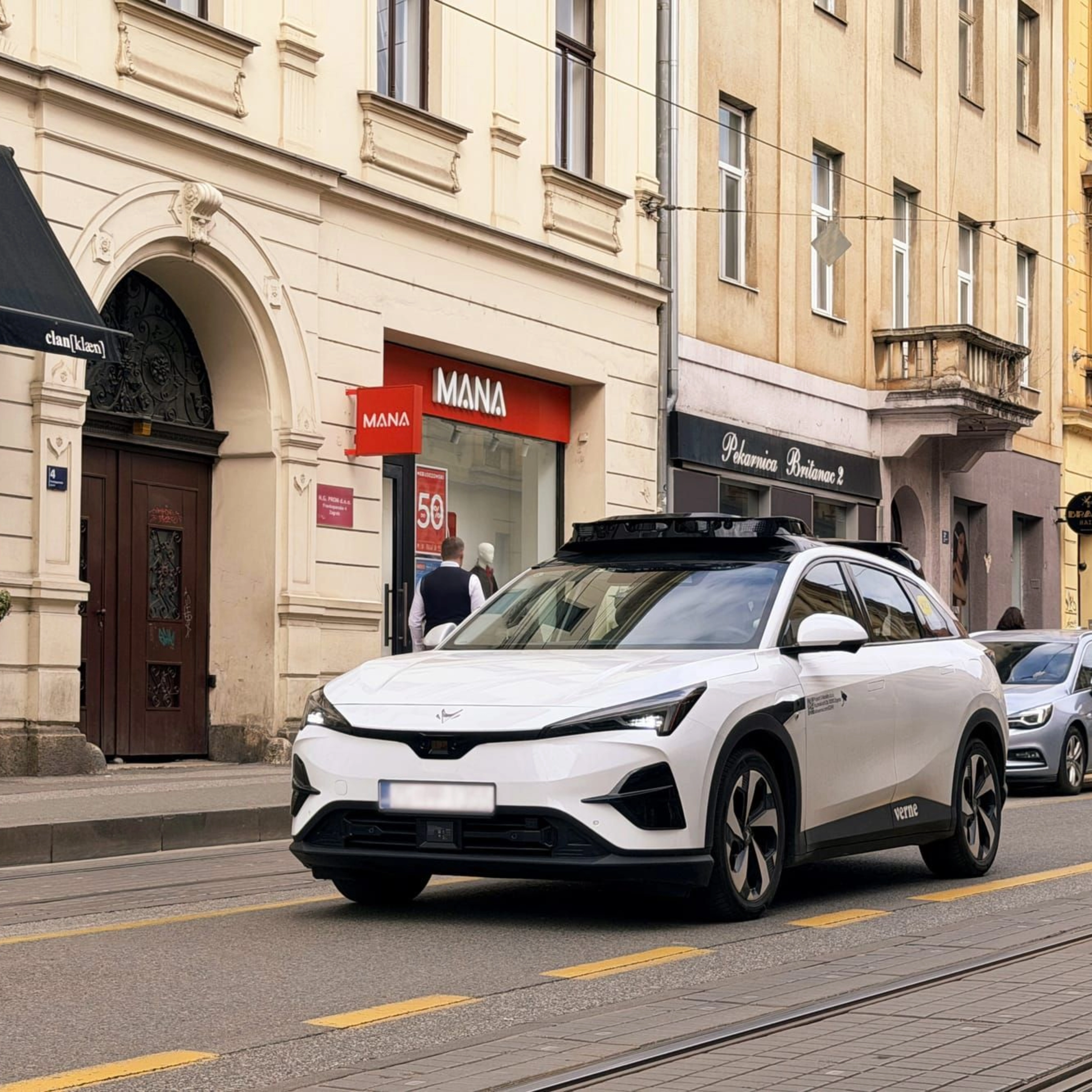 Autonomes Testfahrzeug fährt durch eine Stadtstraße mit Geschäften
