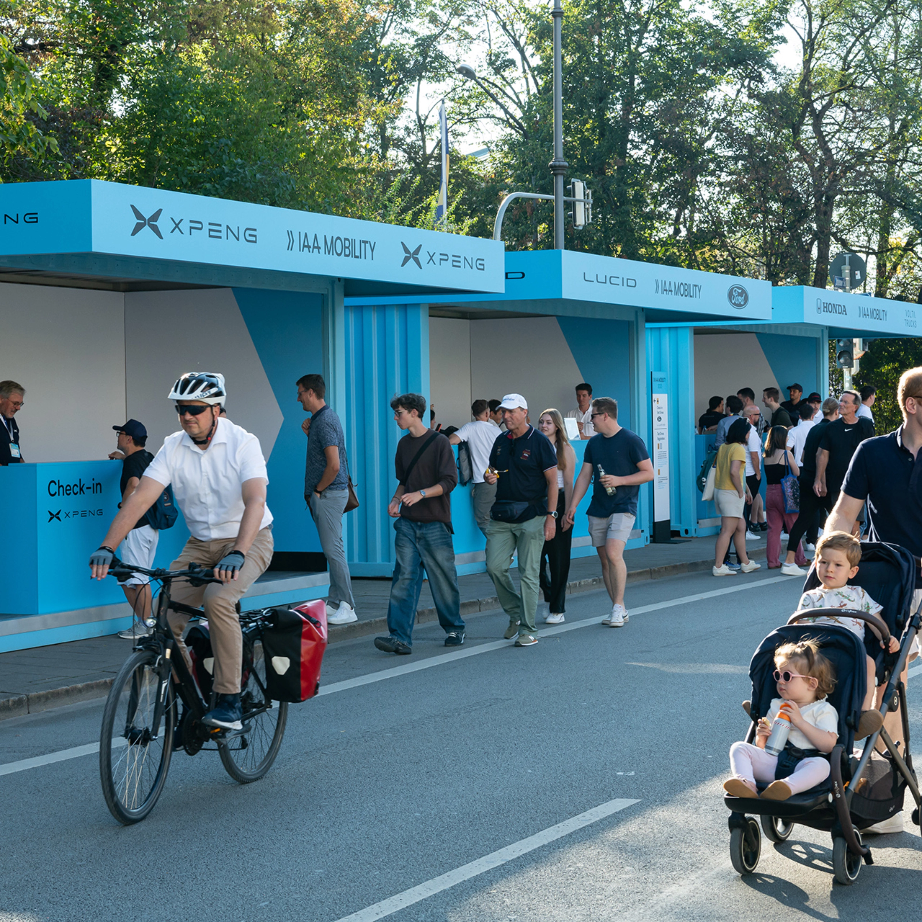 Menschen gehen und fahren mit dem Fahrrad an IAA Mobility Check-in-Ständen auf einer gesperrten Straße vorbei.