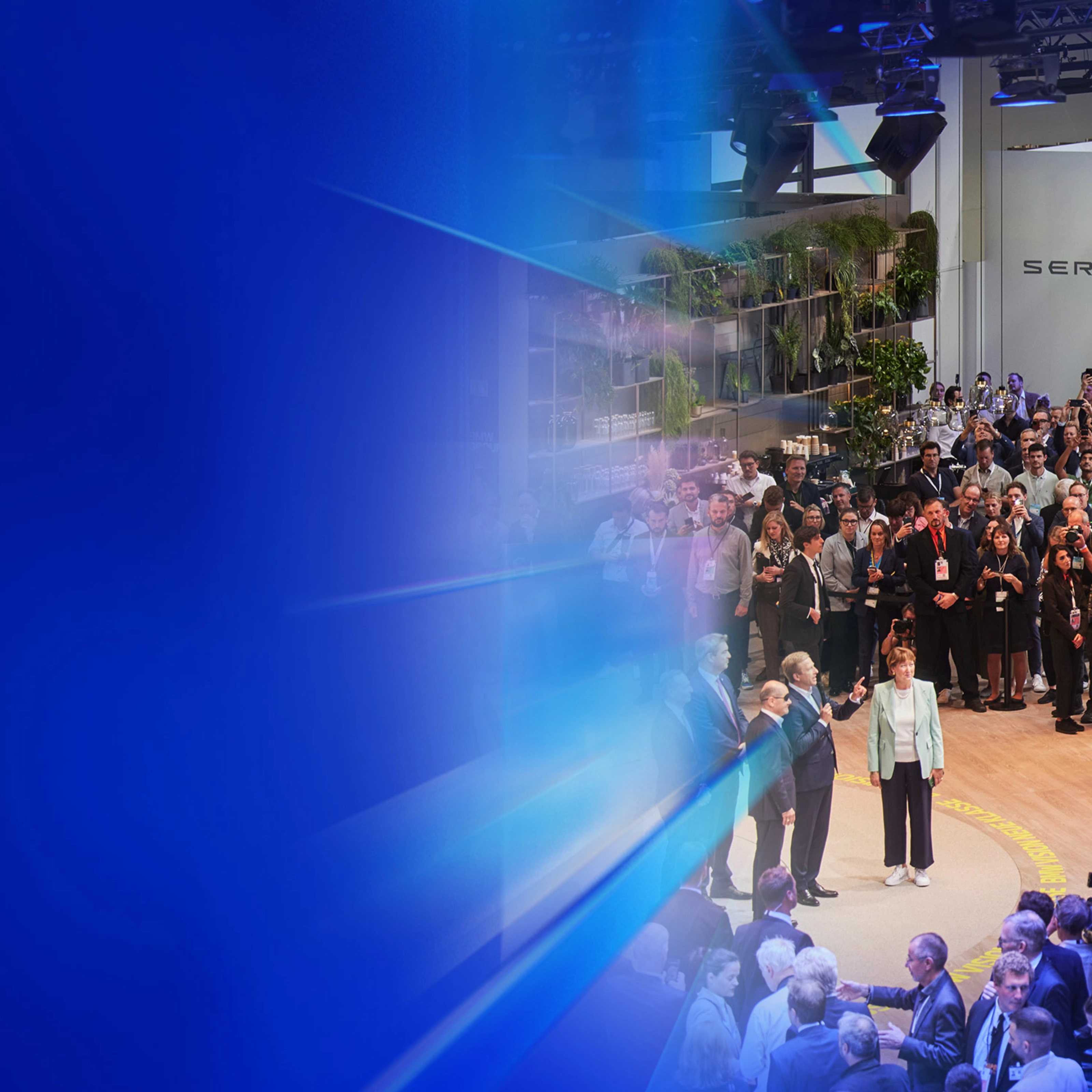 Menschenmenge und Presse auf einer Autoausstellung mit dem Text „5 Gründe – IAA Summit“.