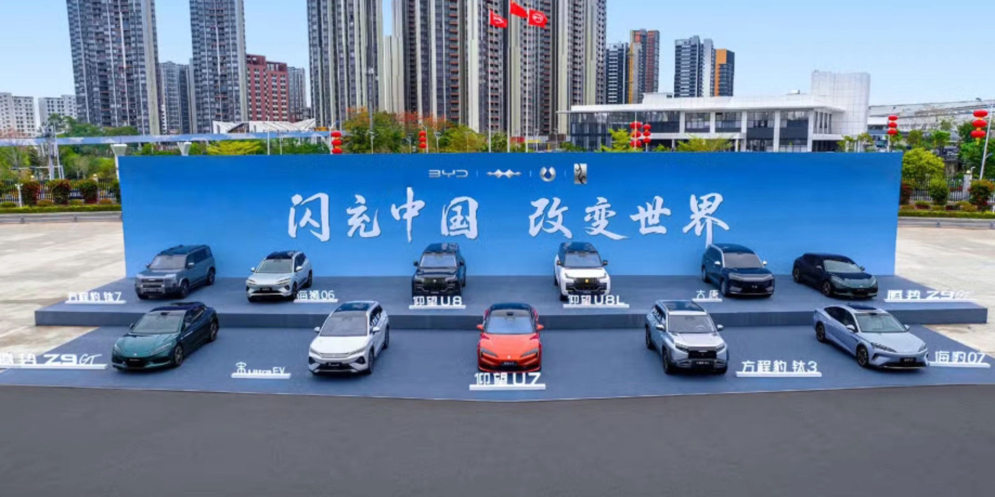 BYD vehicles displayed on a stage outdoors in front of a large promotional backdrop.