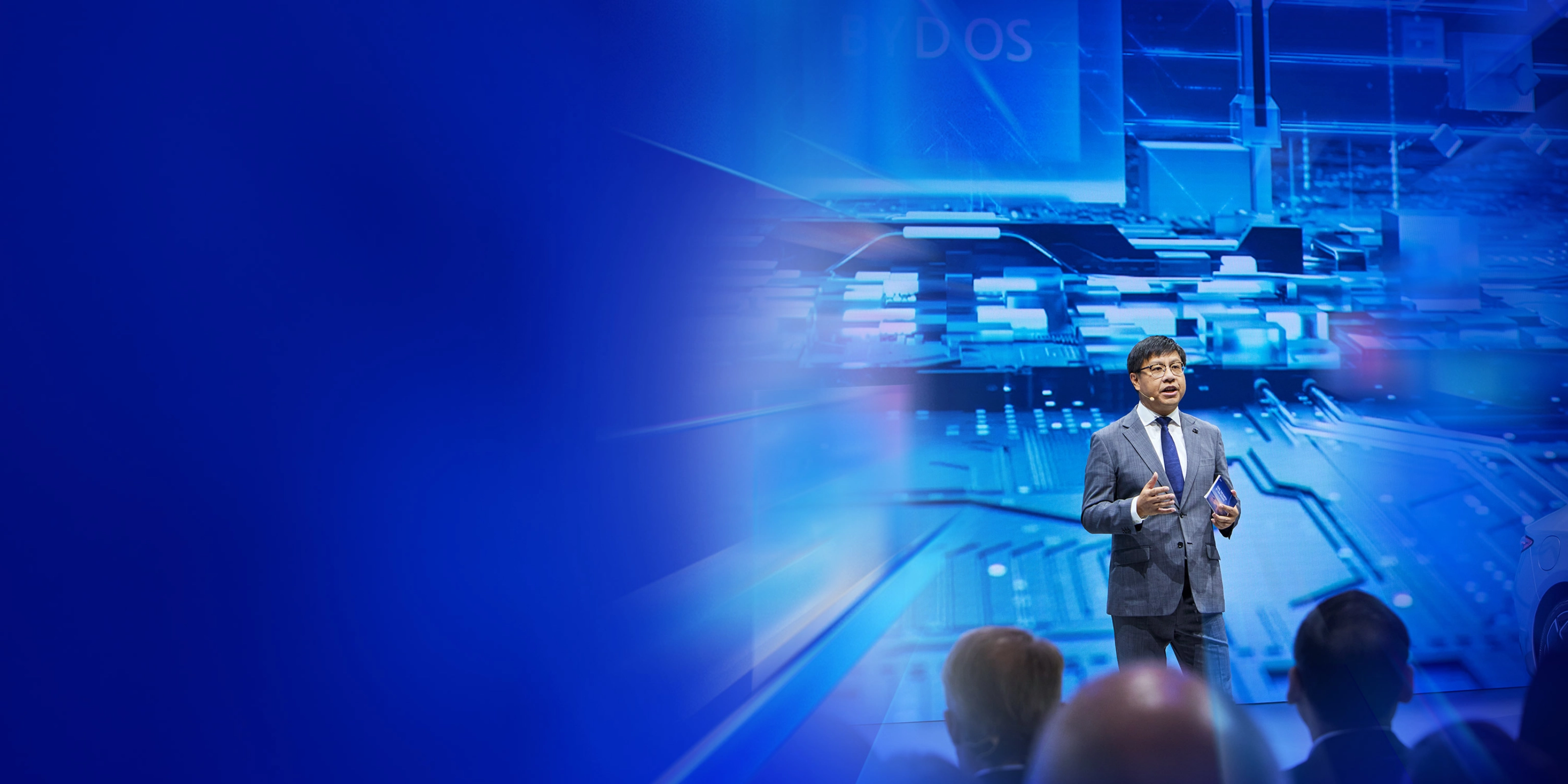 Ein Redner im Anzug spricht auf der IAA Summit Bühne vor digitalem Schaltkreis-Hintergrund.
