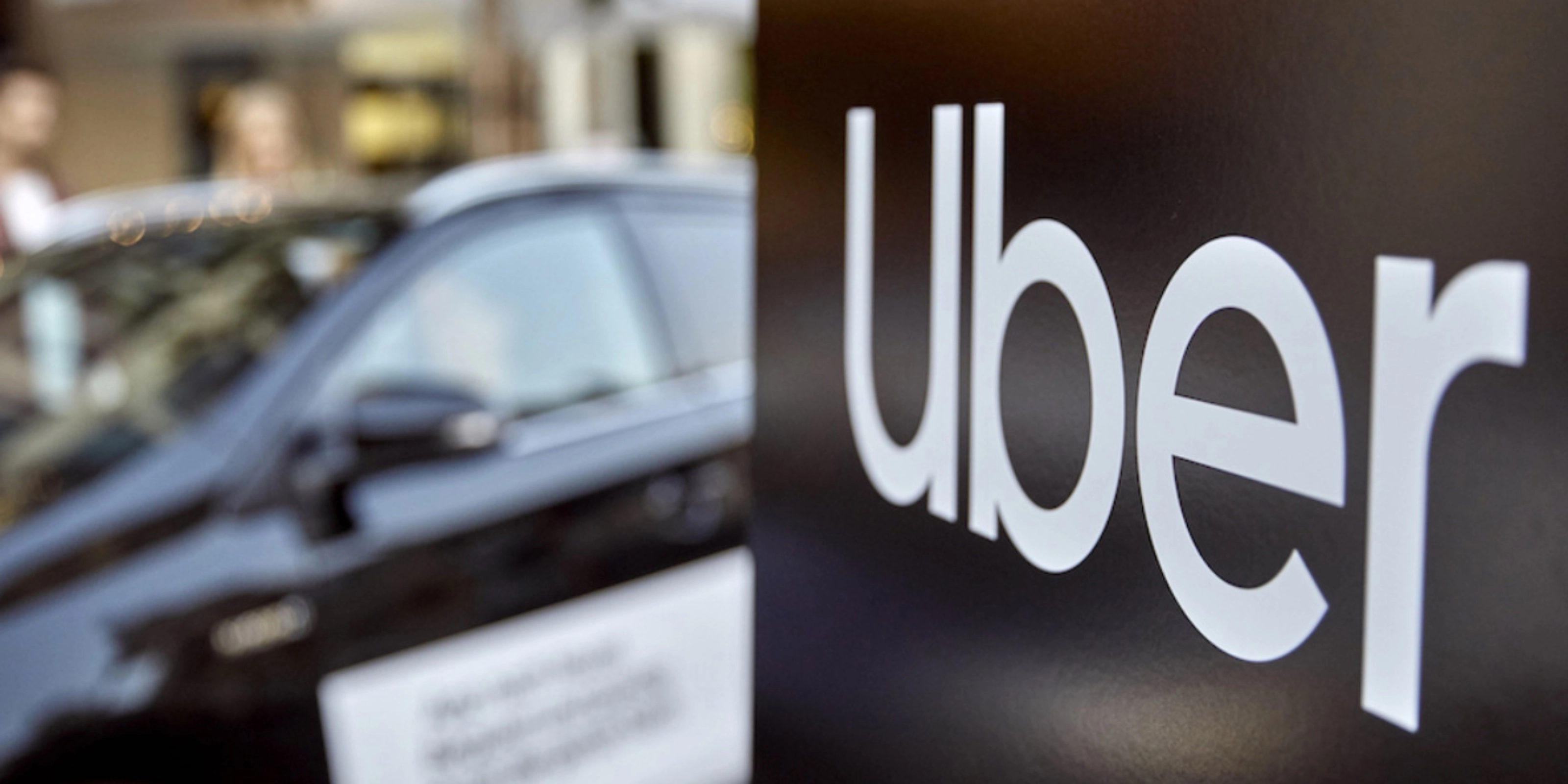 Uber-Logo auf einem Schild, dahinter unscharf ein Auto.