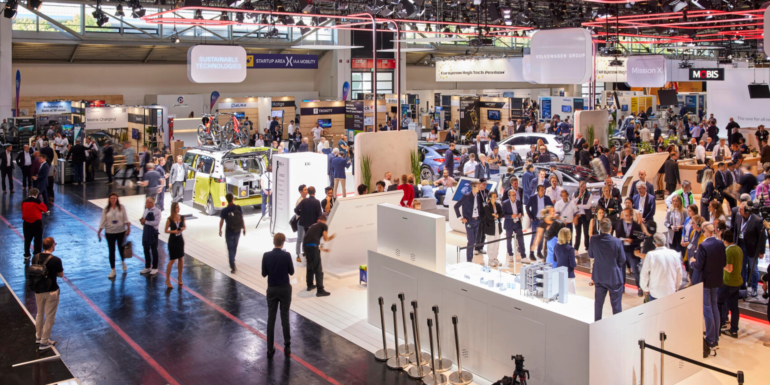 Busy exhibition hall at IAA Mobility 2023 featuring multiple booths, vehicles, and technology displays, with many visitors engaging and walking through the space.