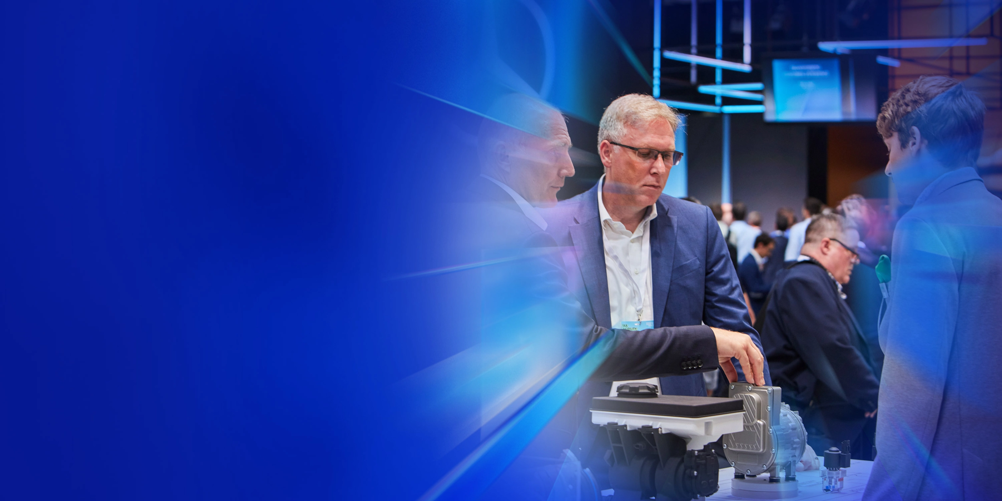 Drei Männer begutachten ein technisches Bauteil auf einer Messe beim IAA Summit.