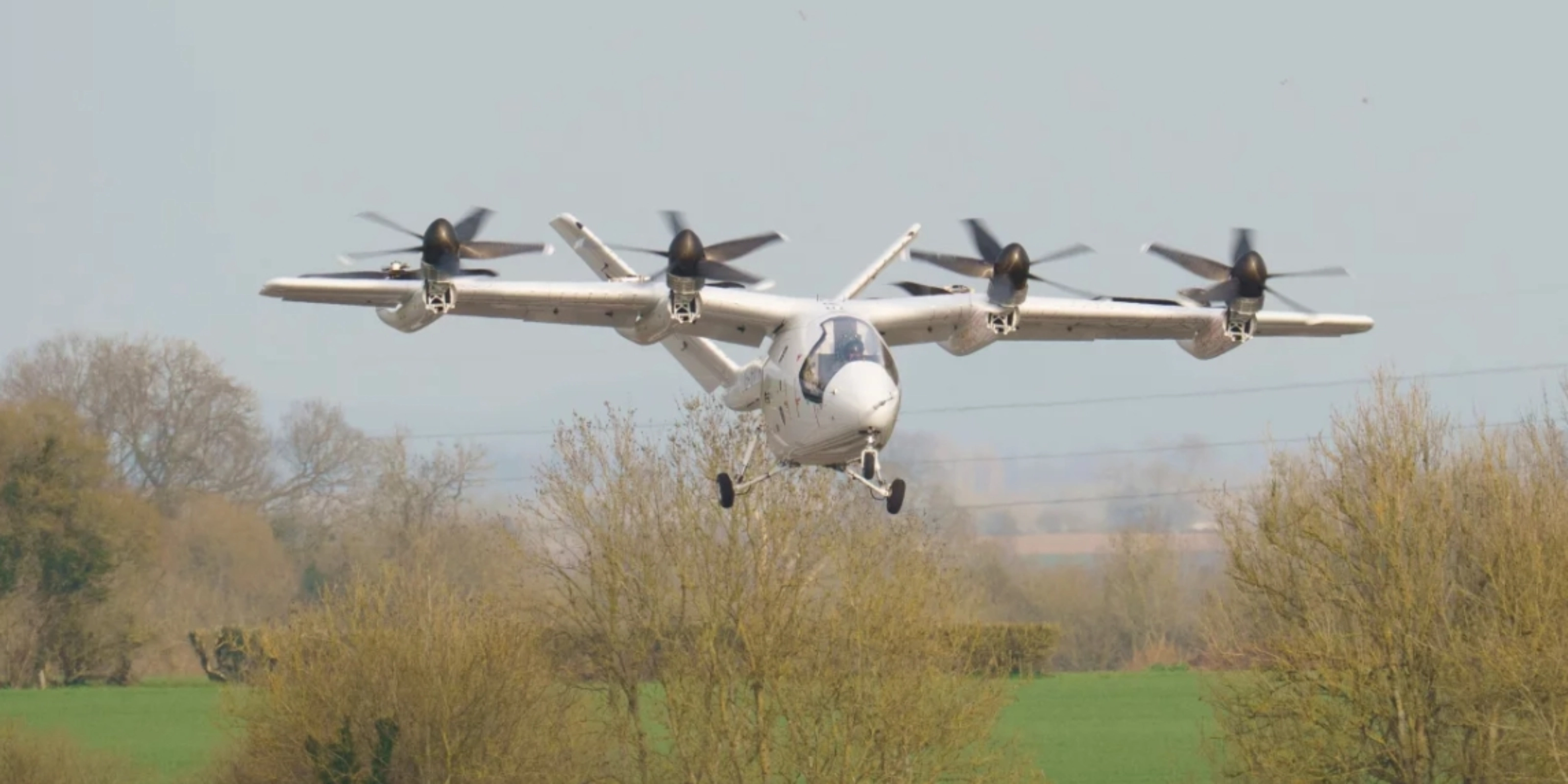 Electric aircraft with multiple rotors flying over trees.