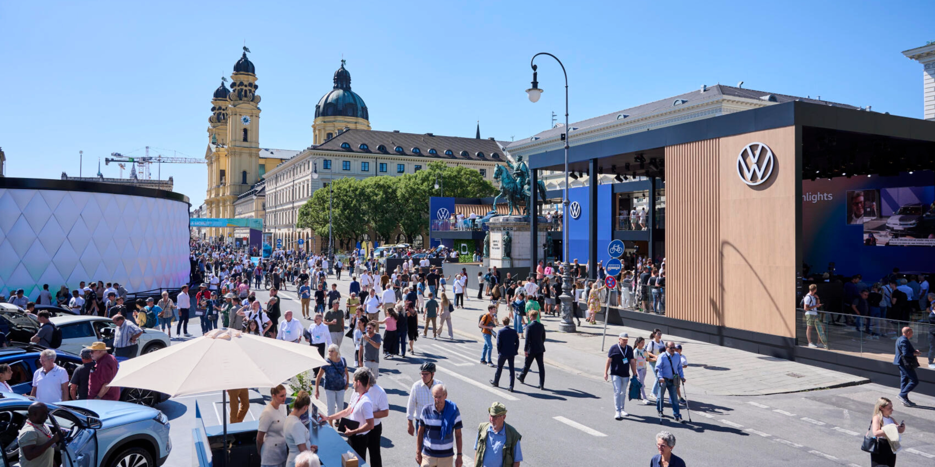 Menschen besuchen eine Outdoor-Mobilitätsmesse mit Ständen und historischen Gebäuden.