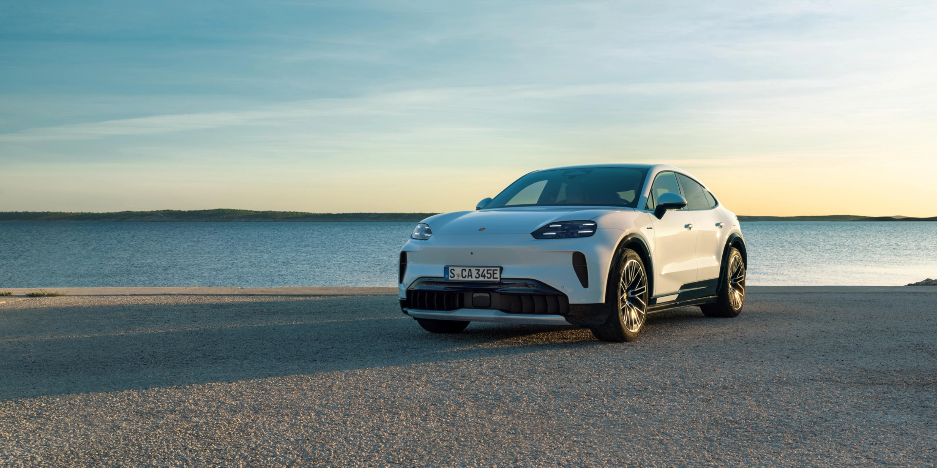 Weißer Porsche steht am Wasser bei Sonnenuntergang.