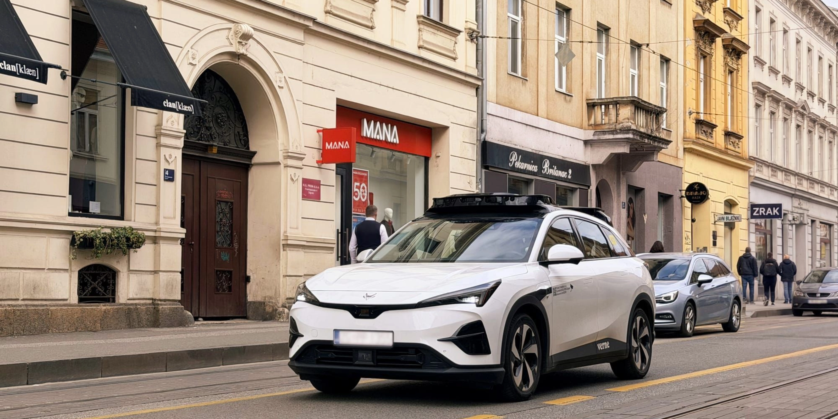 Autonomes Testfahrzeug fährt durch eine Stadtstraße mit Geschäften