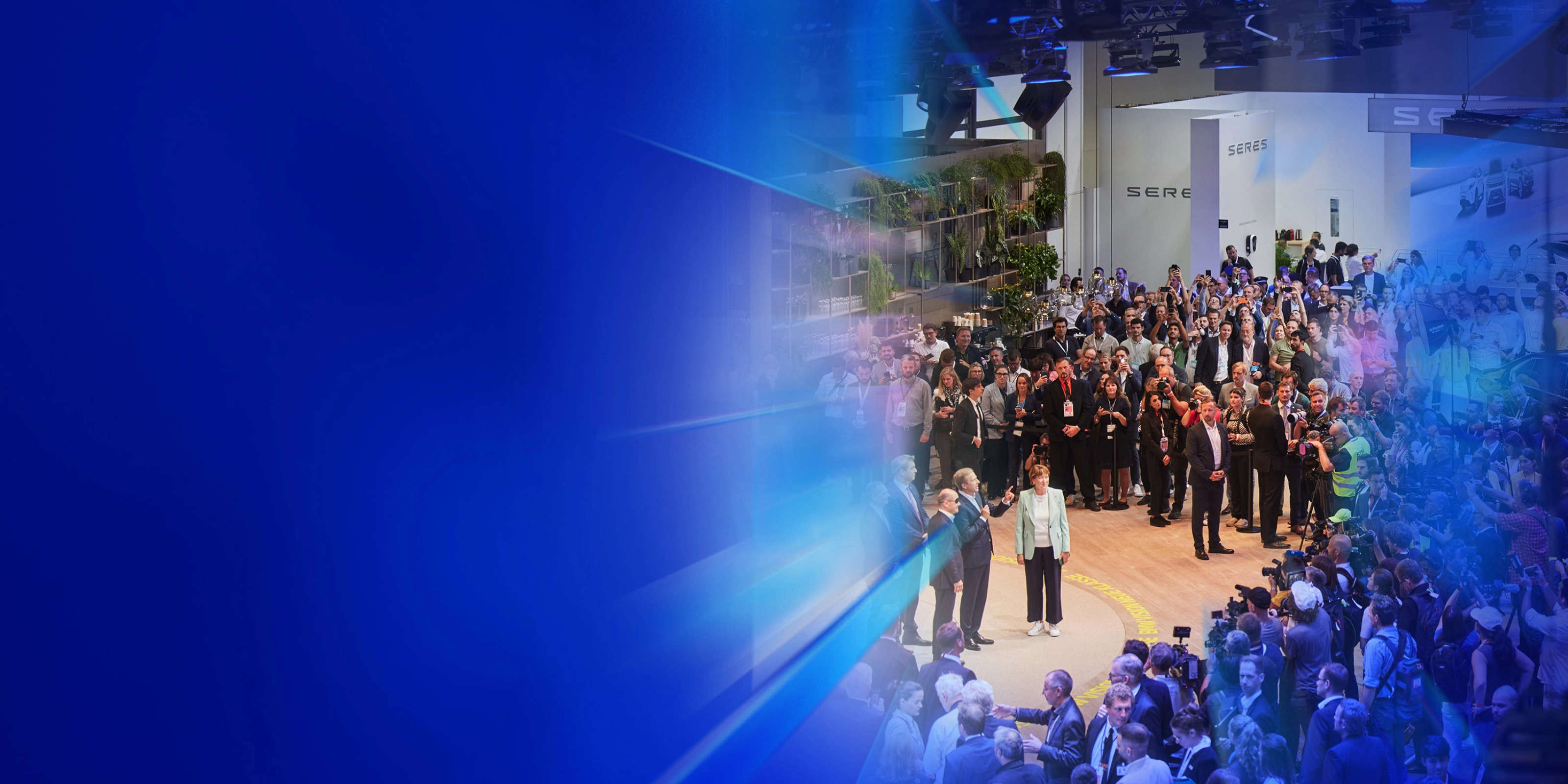 Menschenmenge und Presse auf einer Autoausstellung mit dem Text „5 Gründe – IAA Summit“.