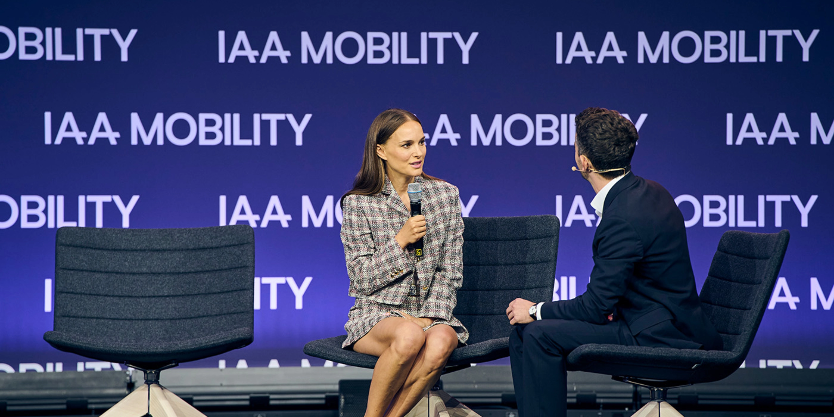 Natalie Portman bei einem Live-Bühneninterview auf der IAA Mobility, sitzend neben einem Moderator vor einer Bühne mit Veranstaltungslogo.