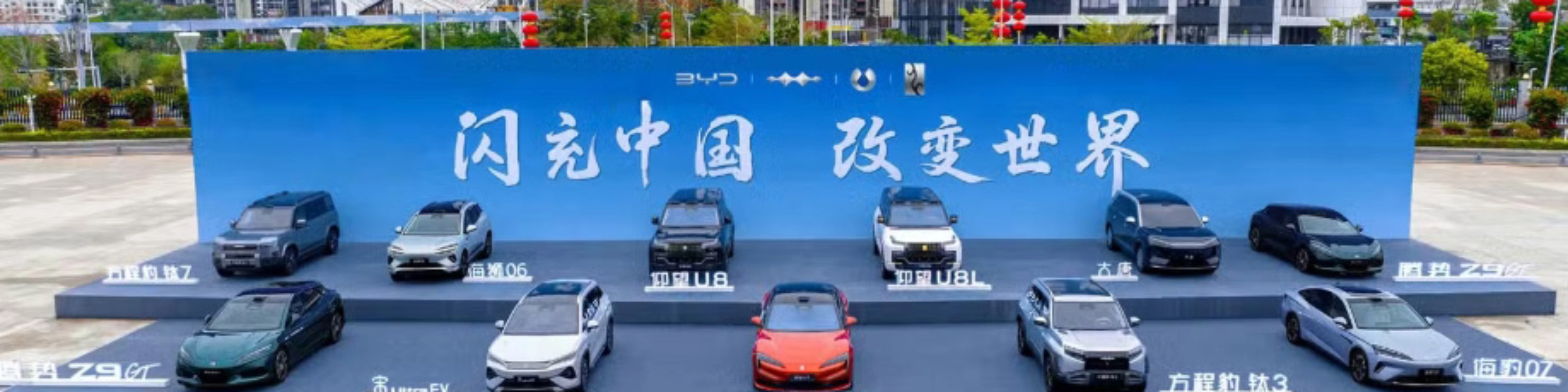 BYD vehicles displayed on a stage outdoors in front of a large promotional backdrop.