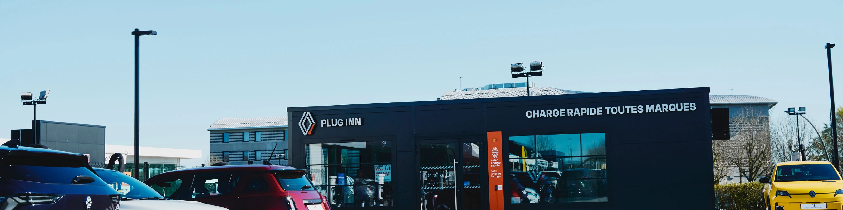 Außenansicht einer Plug-Inn-Schnellladestation mit mehreren geparkten Autos.
