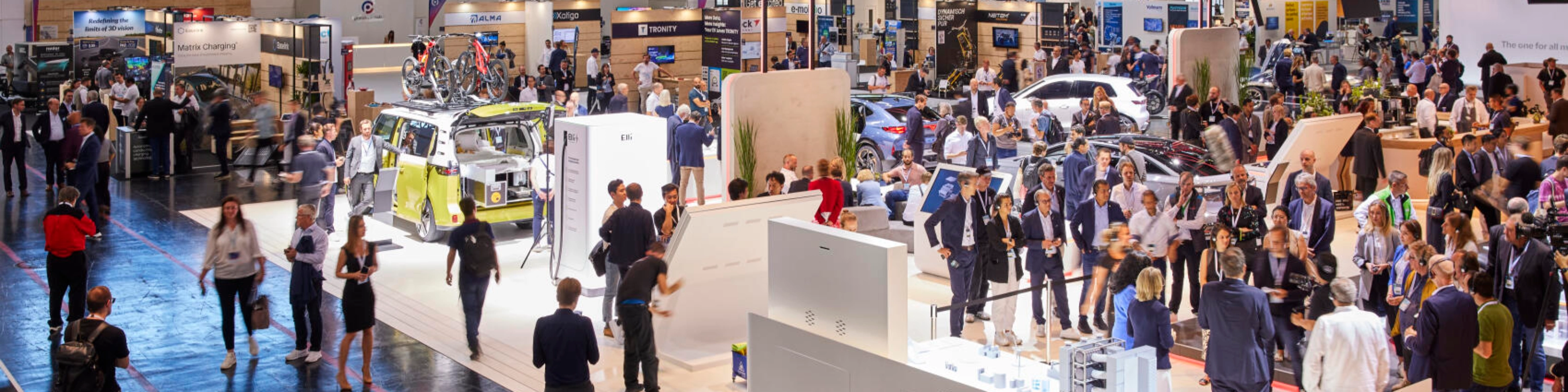 Busy exhibition hall at IAA Mobility 2023 featuring multiple booths, vehicles, and technology displays, with many visitors engaging and walking through the space.
