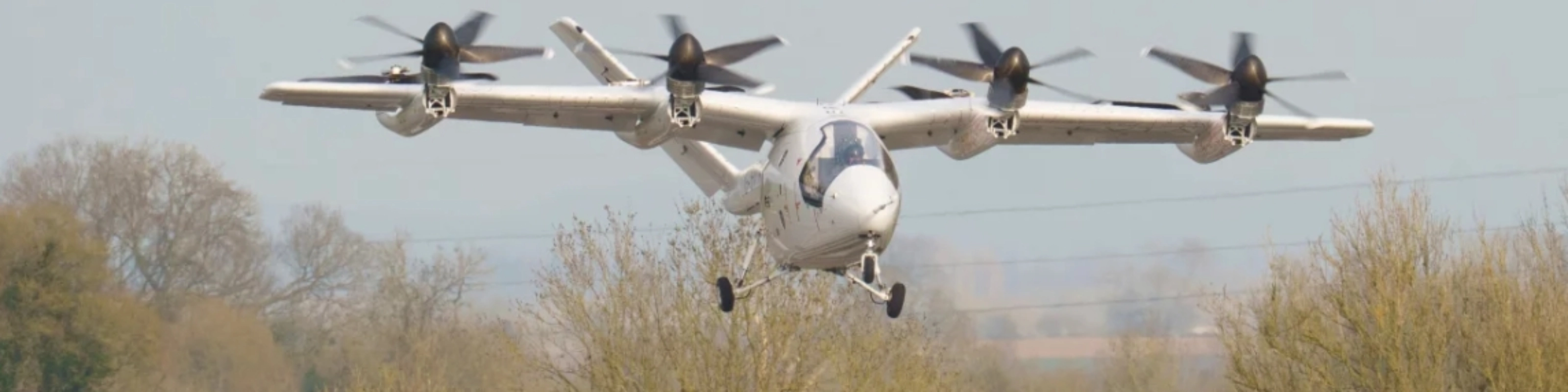 Electric aircraft with multiple rotors flying over trees.