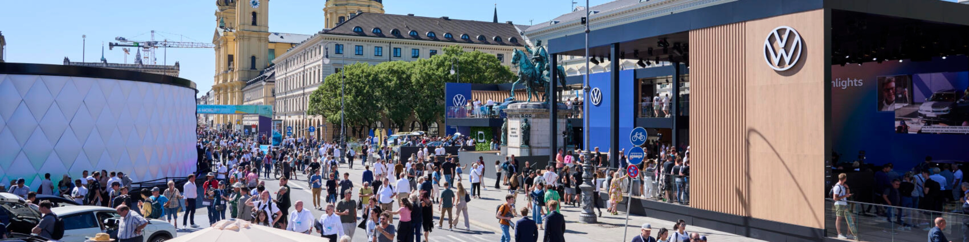 Menschen besuchen eine Outdoor-Mobilitätsmesse mit Ständen und historischen Gebäuden.